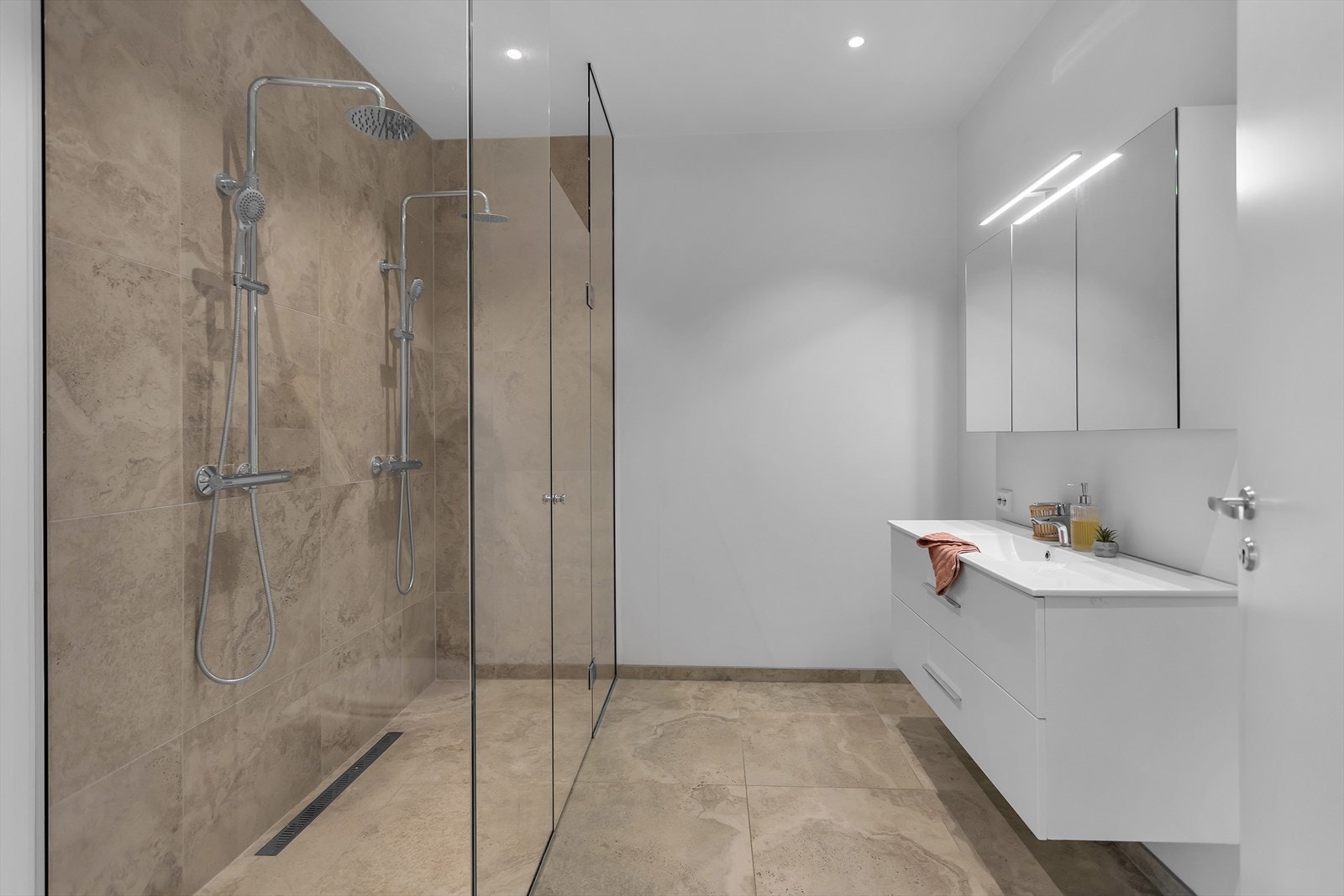Lekkert og stilfullt baderom med en imponerende dusjnisje som har en romslig dusjsone med heldekkende glassvegger og doble dusjhoder med regndusj, som gir en eksklusiv spa-følelse. Gulvet og dusjsonen er belagt med flotte 60x60 fliser. Galleribilde