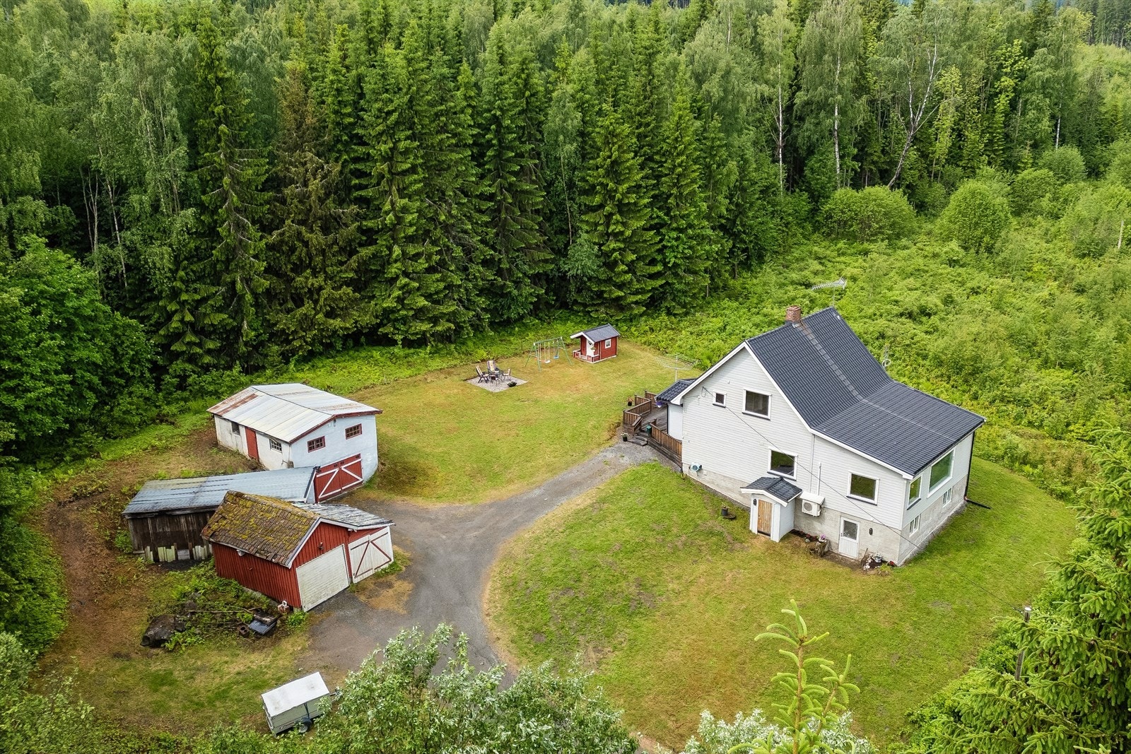 Oversikt over den romslige eiendommen med enebolig, hage og tre garasjebygg. Galleribilde
