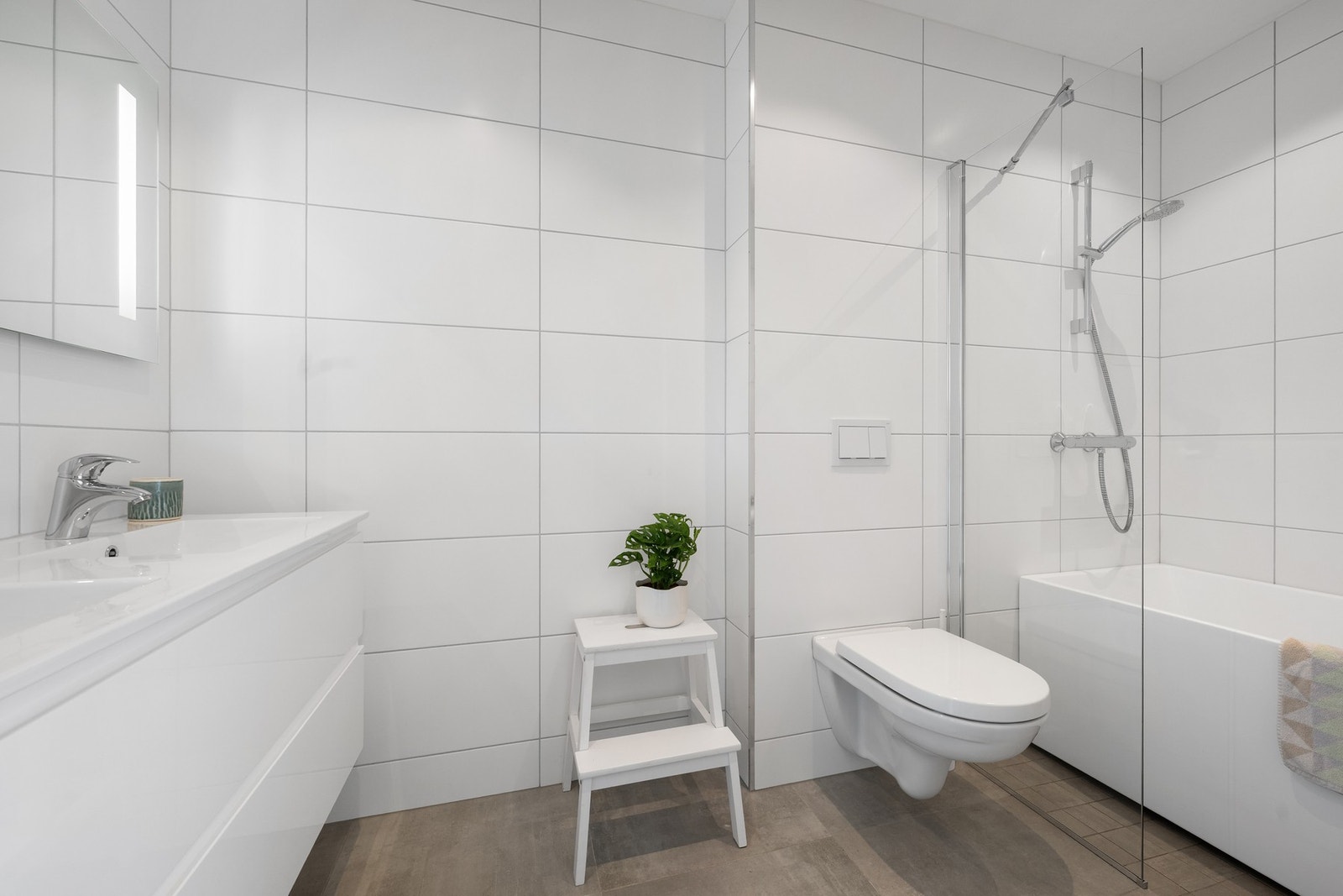 Badet er innredet med badekar med glassvegg, veggmontert toalett og balansert ventilasjon, en praktisk løsning for både småbarnsfamilier og gjester. Galleribilde