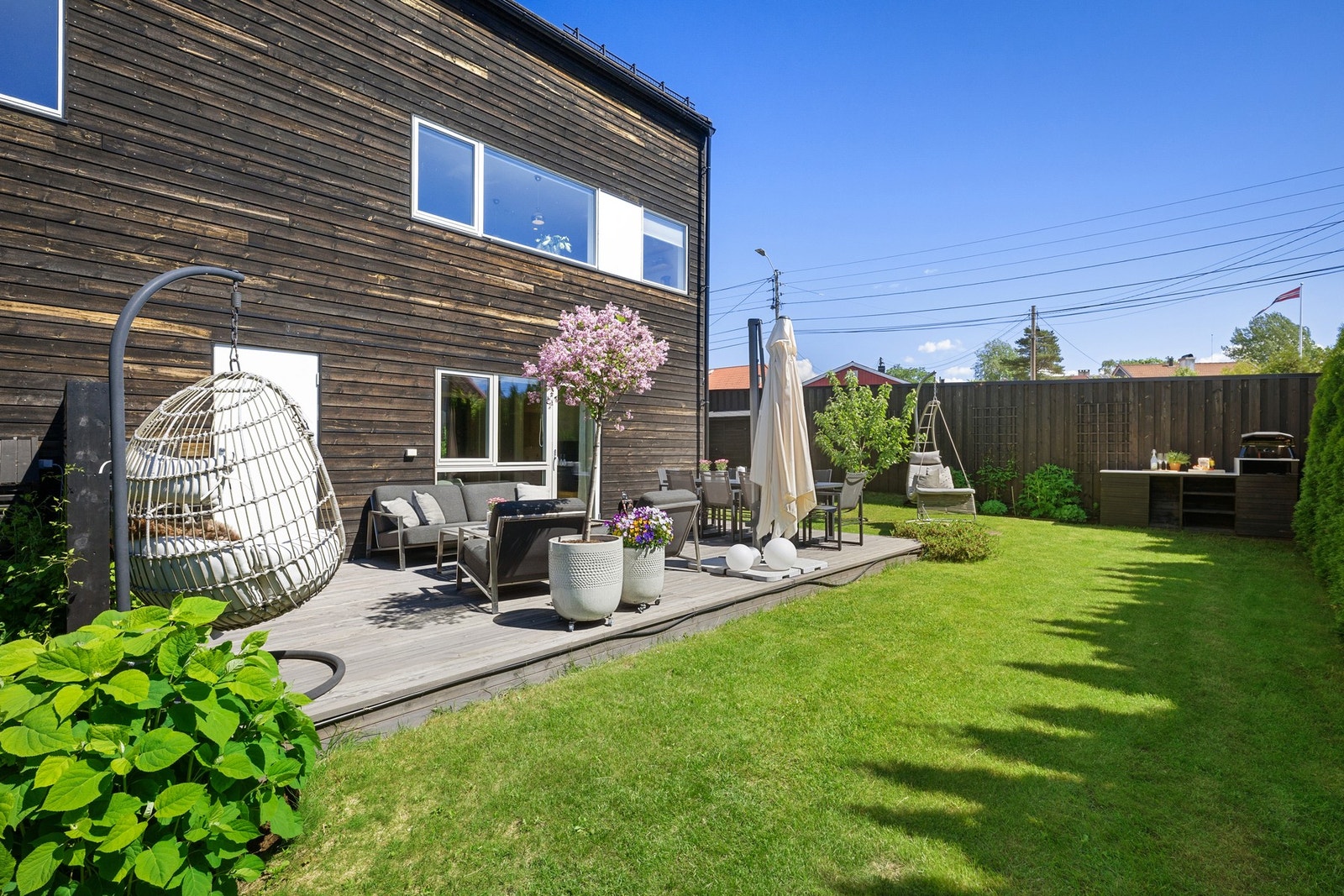 Den frodige hagen er pent opparbeidet med plen, beplantning og stor platting, og gir en lun og skjermet ramme for både hverdag og sosiale sammenkomster. Galleribilde