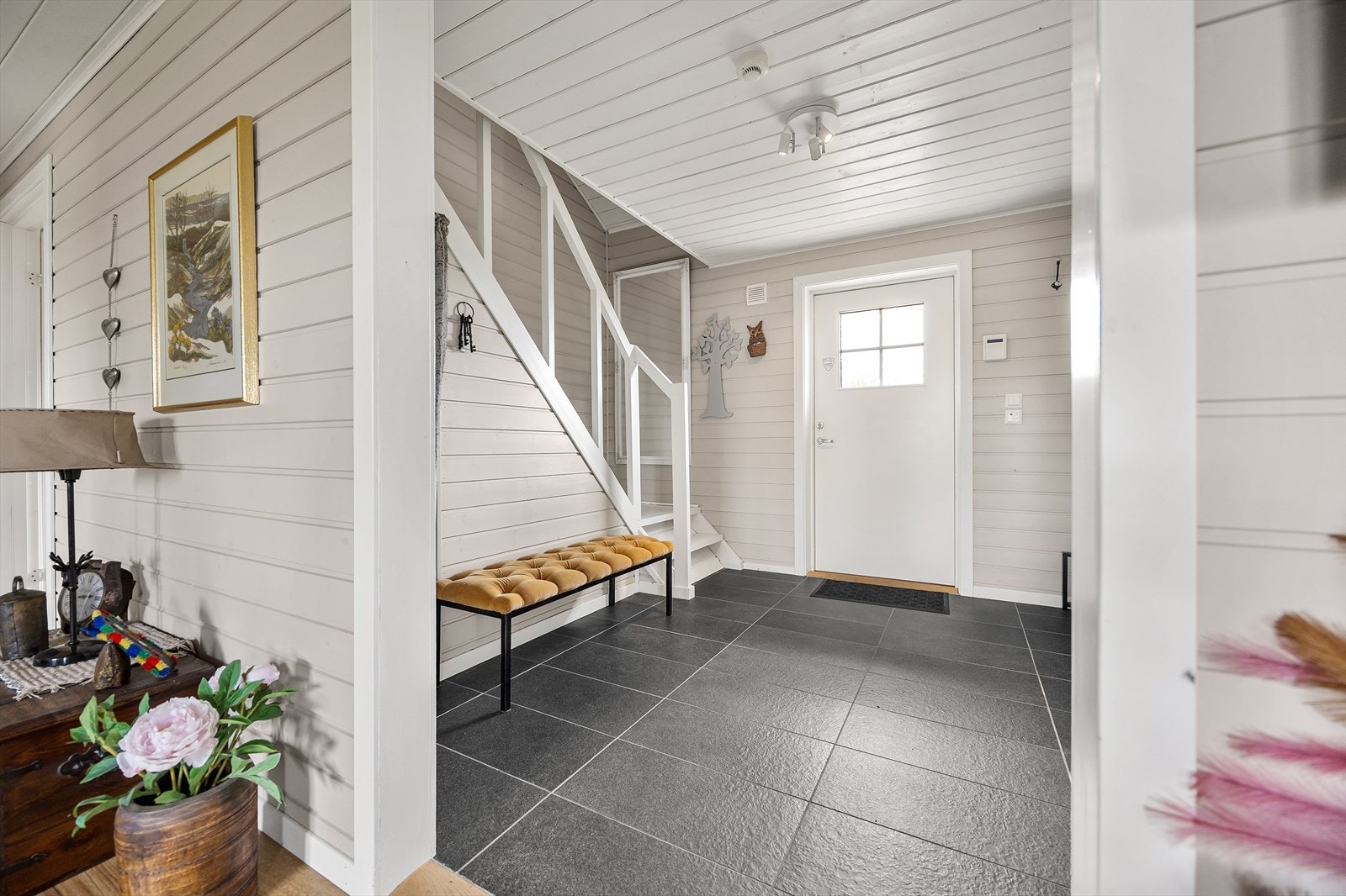 Entreen er innbydende med mørke fliser på gulvet, lysmalte vegger i liggende panel og hvitmalt panelhimling. Galleribilde