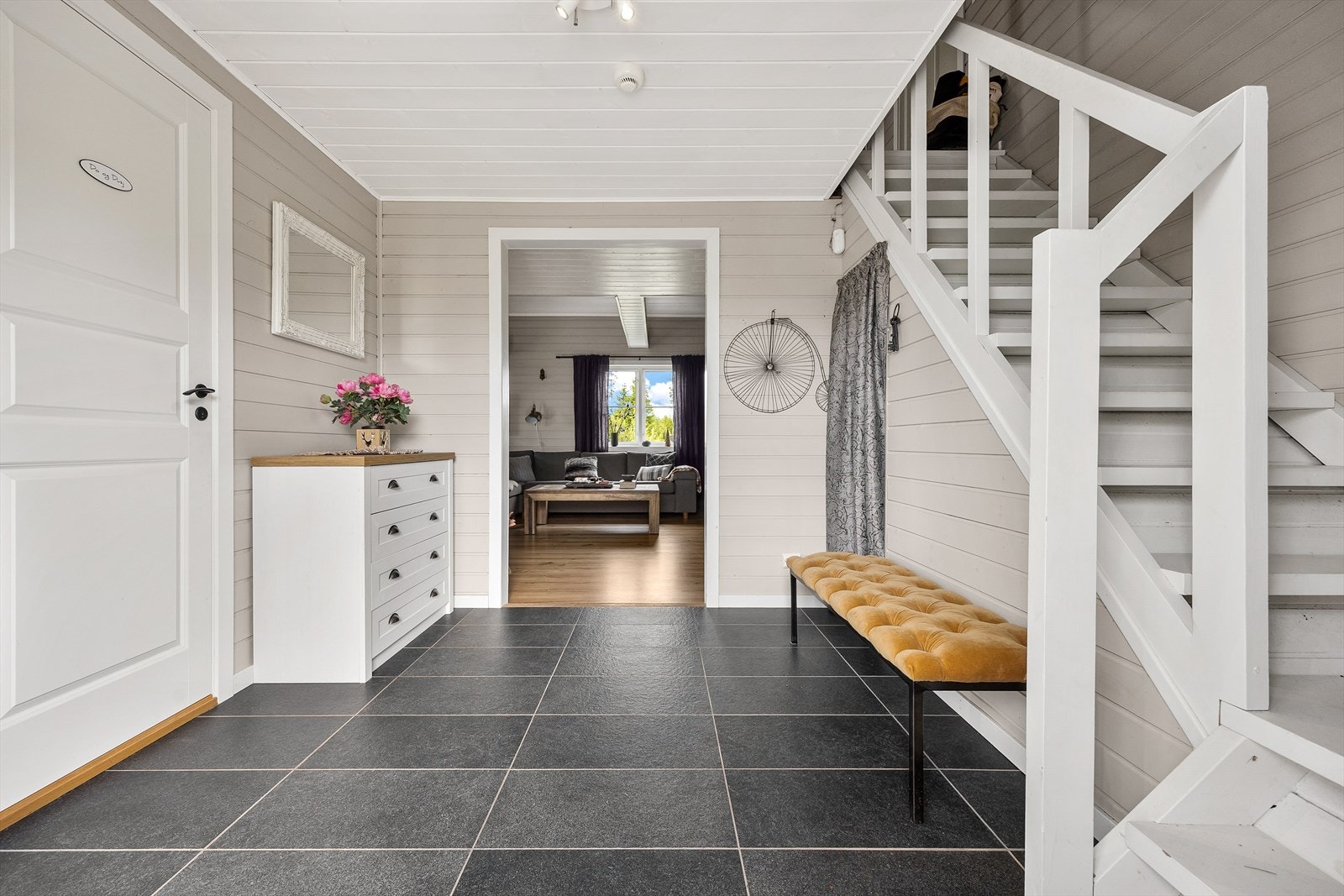 Fra entreen fører en hvitmalt trapp opp til hemsen og en bred døråpning inn til stue/kjøkken. Det er kott under trappen og god plass til garderobemøbler. Galleribilde