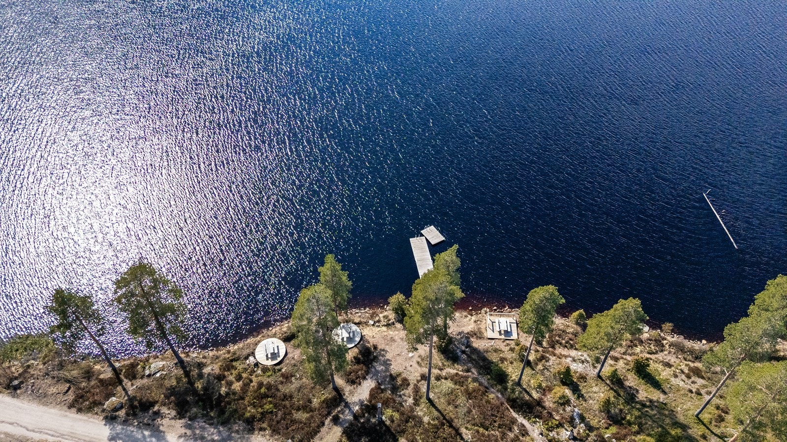 Fra hytta er det en kort rusletur ned til vannet. Her er det felles brygger og badeplasser, samt felles terrasser med benker og bord. Galleribilde