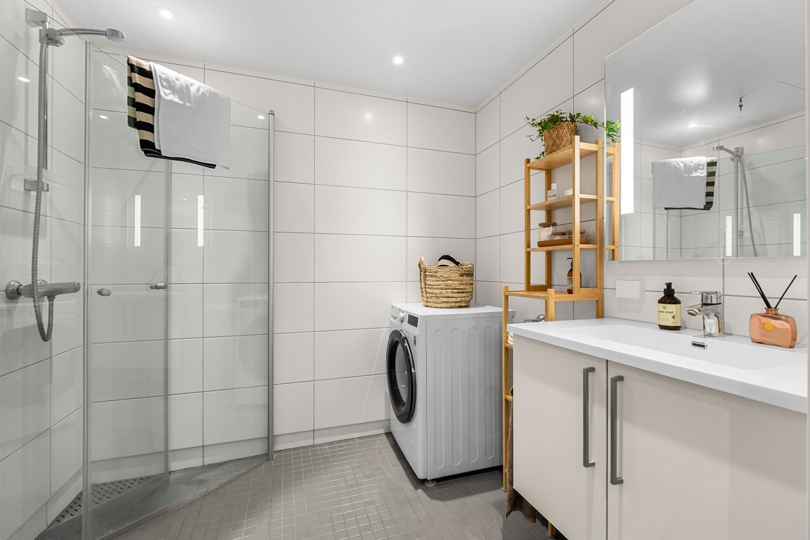Badet har moderne innredning og opplegg for vaskemaskin. Dusjhjørnet er også plassbesparende, med innfellbare glassdører. Galleribilde