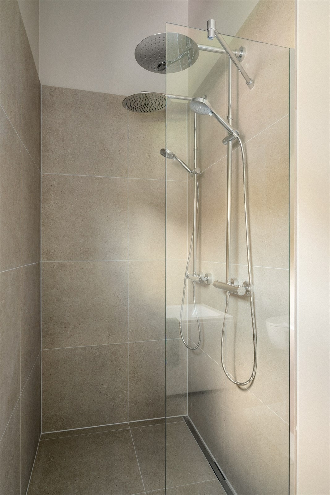 Den romslige dobbeldusjsonen er utført med store fliser, glassvegg og moderne armaturer som gir badet et tidløst uttrykk. Galleribilde
