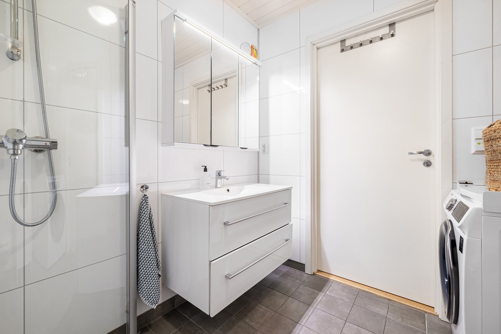 Badet i denne etasjen har flislagt betonggulv og vegger med Fibo veggpanel. Rommet er innredet med servant med underskap og skuffer, speil, toalett og dusjhjørne med glassdører. Galleribilde