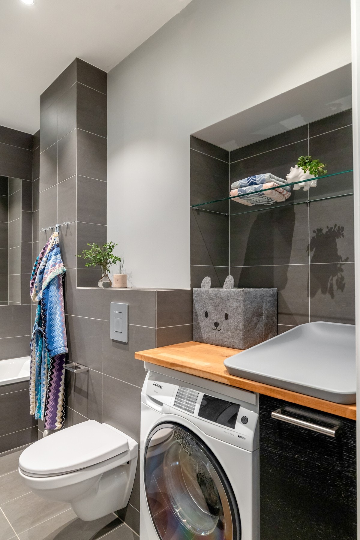 Videre er badet utstyrt med vegghengt toalett og opplegg for vaskemaskin under plassbygget benkeplate og skap med god plass til oppbevaring. Galleribilde