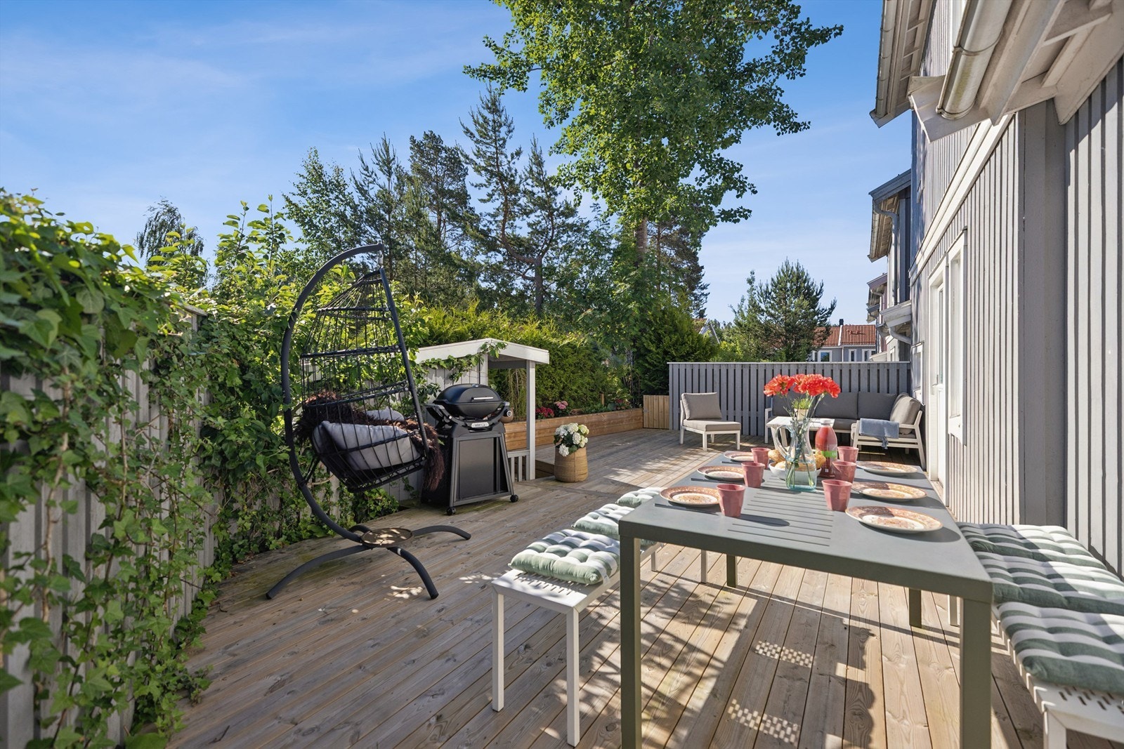 Terrassen er en flott og usjenert uteplass med tredekke, omkranset av hekk, beplantning og gjerde med klatreplanter som skaper en lun og privat ramme. Galleribilde