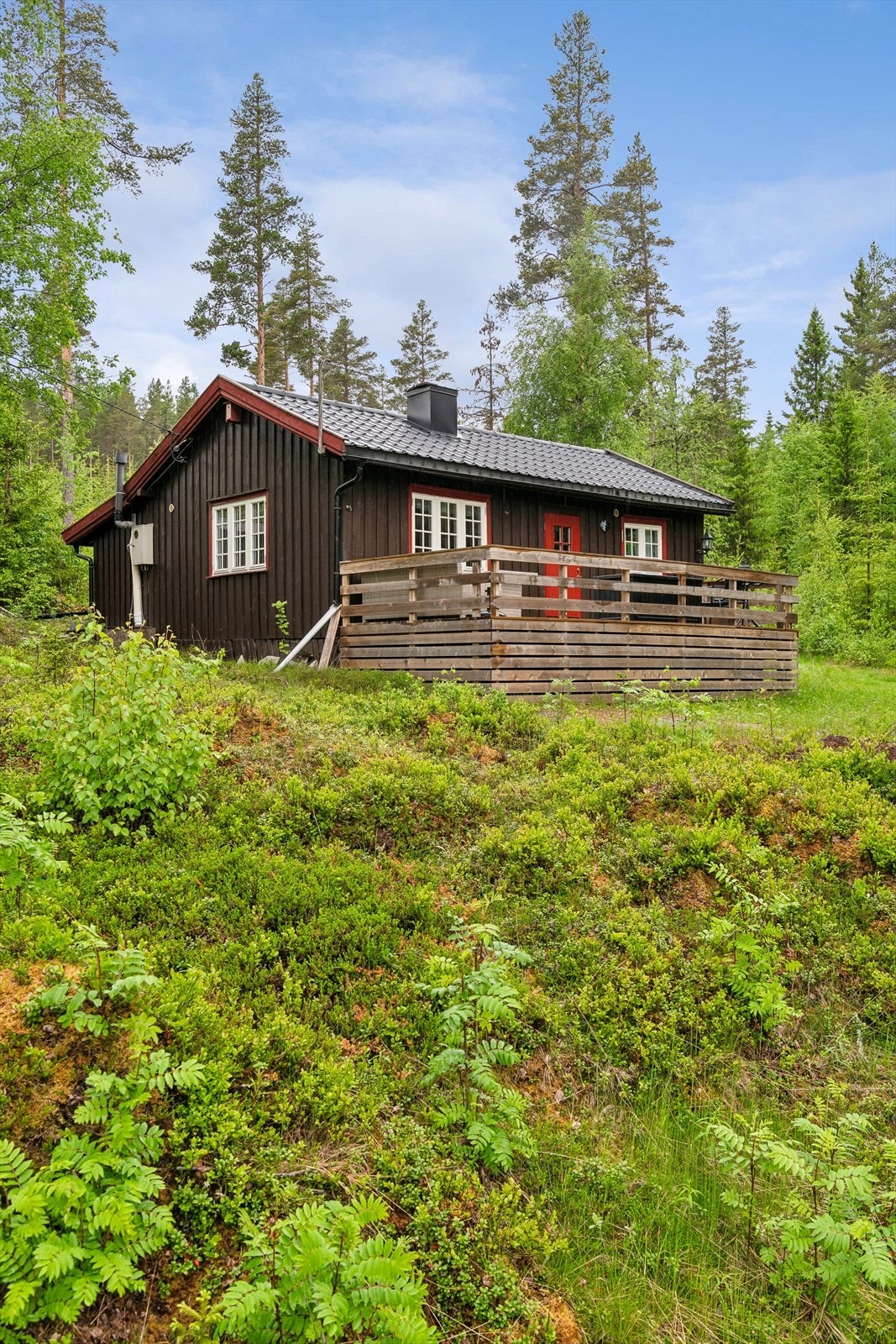 Hytta har stående bordkledning og tak tekket med stålplater. Galleribilde