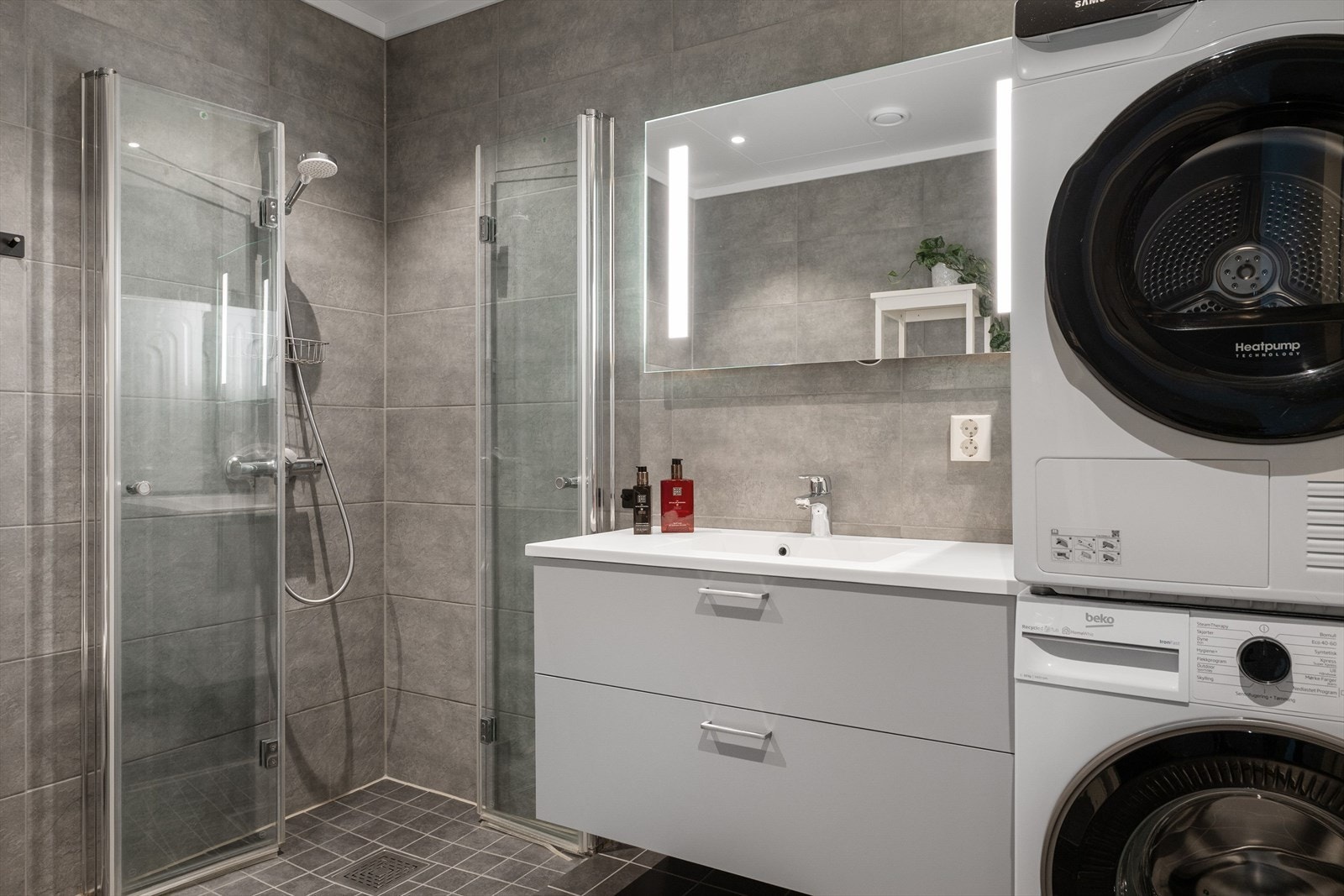 Badet er innredet med nedfelt servant, veggmontert toalett, dusjhjørne med dusjvegger og opplegg for vaskemaskin. Galleribilde