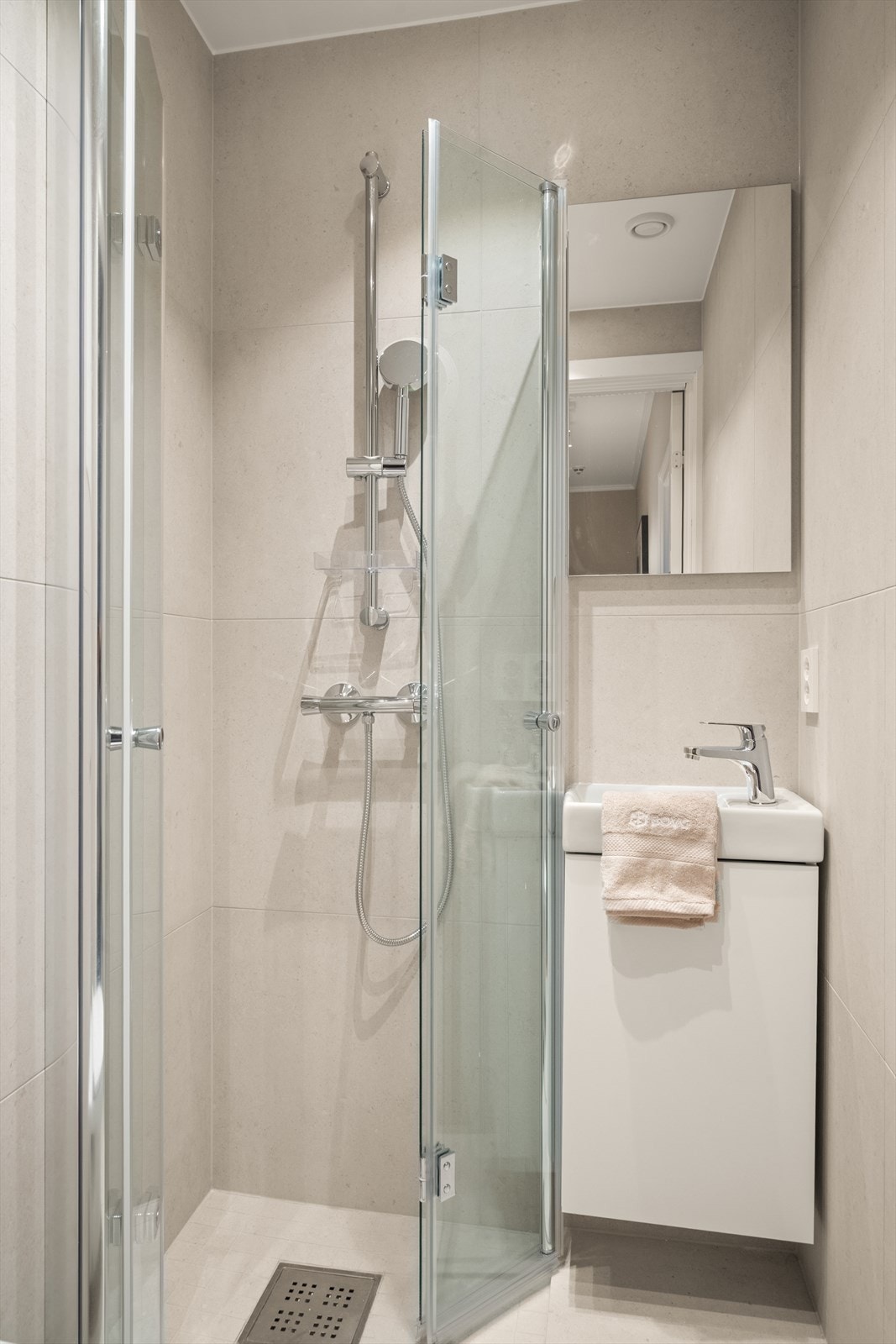 Badet er innredet med dusjhjørne med innfellbare glassdører og vegghengt toalett med innbygget Geberit-sisterne og integrert flomsikring. Baderomsinnredningen består av servantskap med heldekkende servant, ettgrepsbatteri og speil. Galleribilde