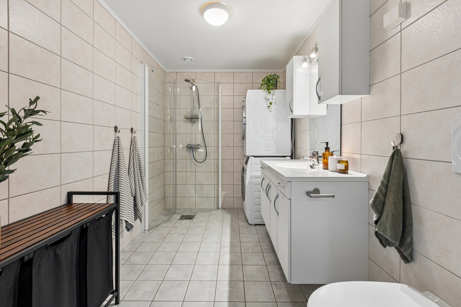 Badet er utstyrt med dusjløsning, vegghengt toalett, servant med innredning og opplegg for vaskemaskin Galleribilde