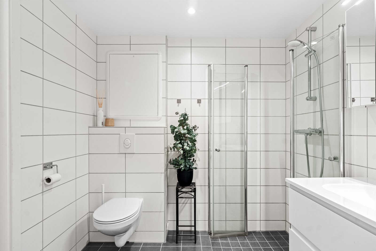 Badet er lyst og delikat med vegghengt toalett og dusjsone med glassvegger. En praktisk løsning med god utnyttelse av arealet. Galleribilde