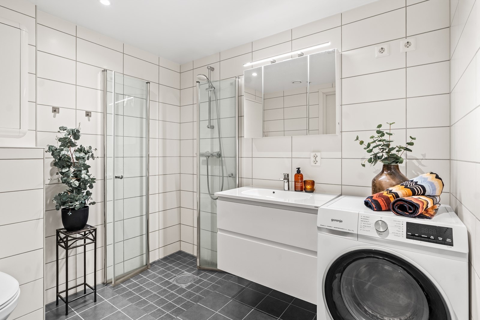 Romslig og moderne bad med flislagte overflater, dusjhjørne og opplegg for vaskemaskin. Badet har en stilren og funksjonell innredning. Galleribilde