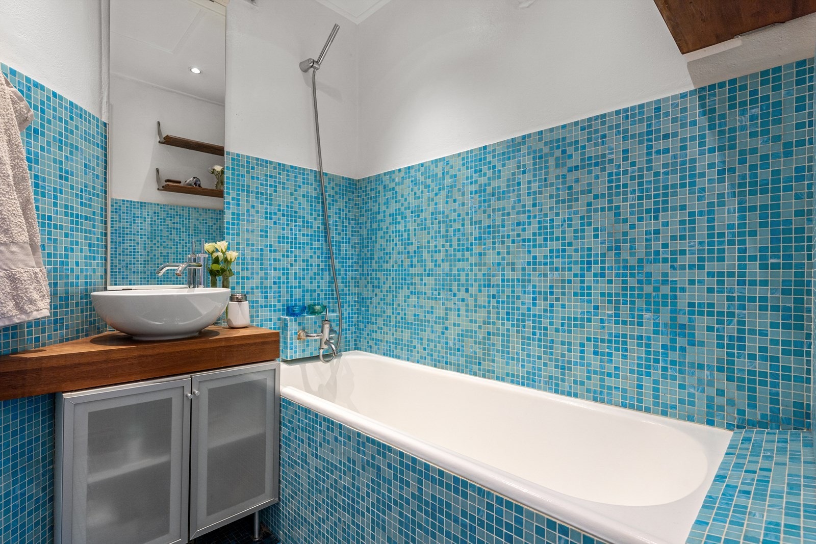 Badet har karakteristiske mosaikkfliser på gulv og vegger, samt et innfliset badekar. Galleribilde