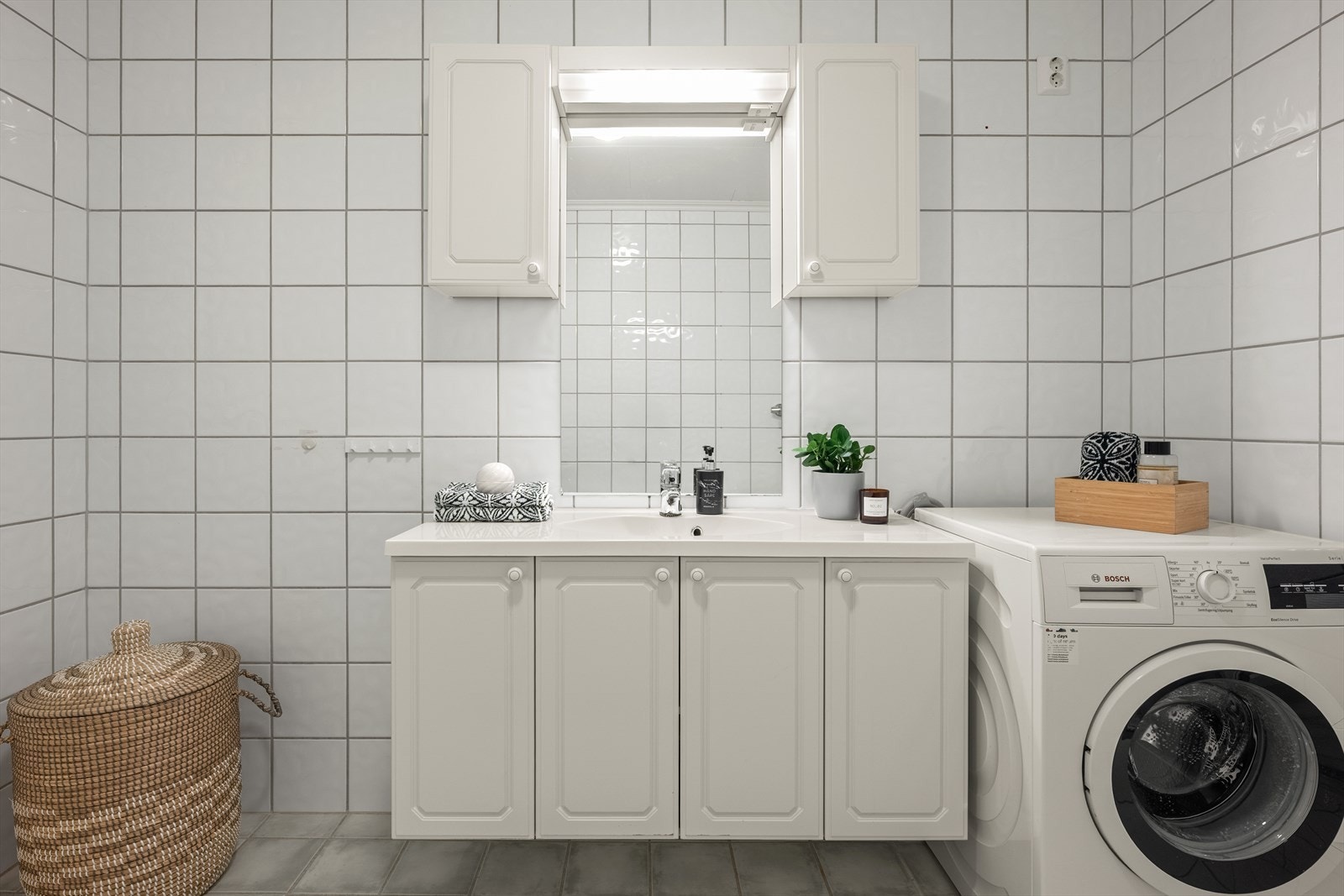 Romslig, flislagt bad med servant i innredning og opplegg for vaskemaskin. Galleribilde