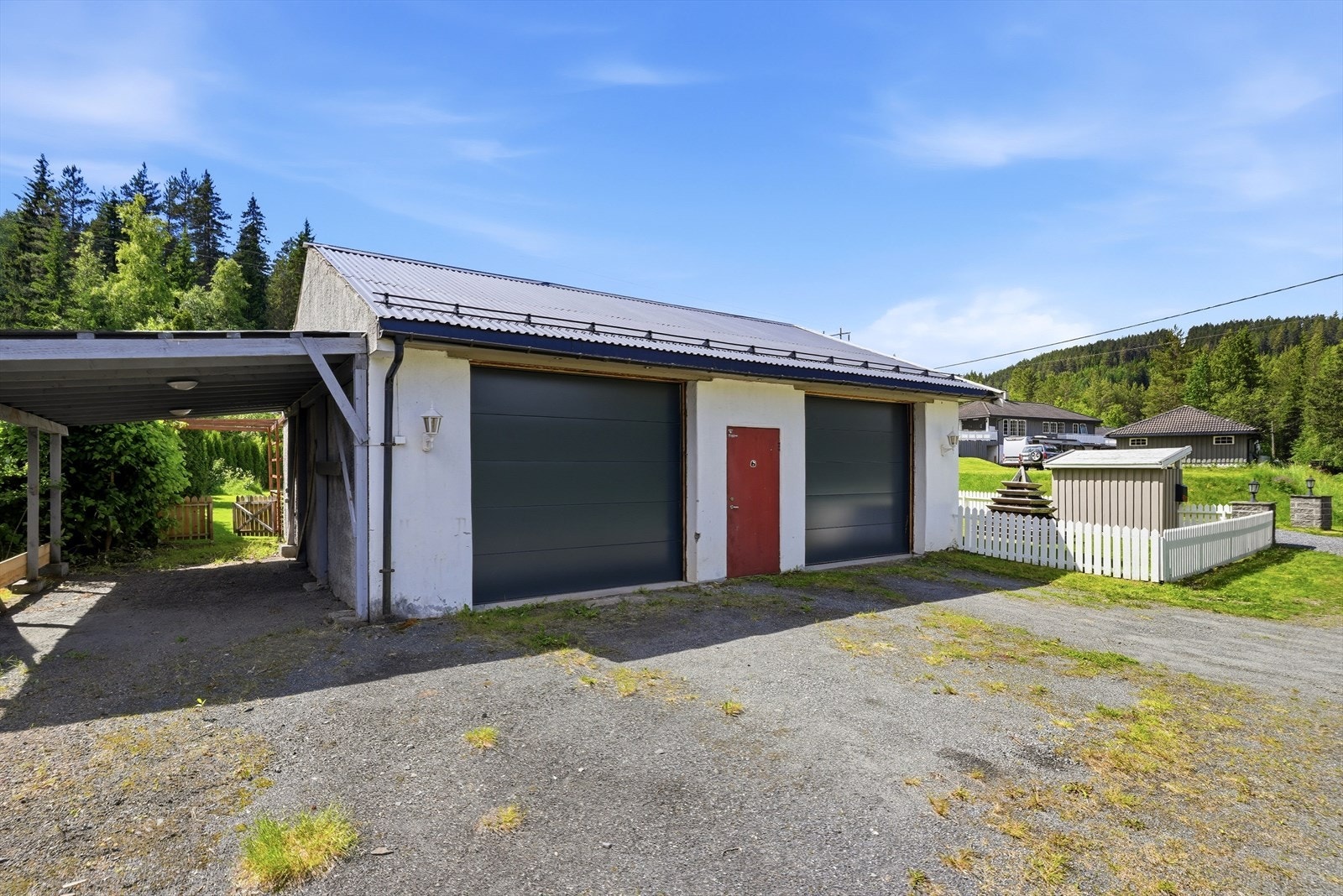 Stor garasjebygning med to garasjeporter og tilhørende carport. Galleribilde