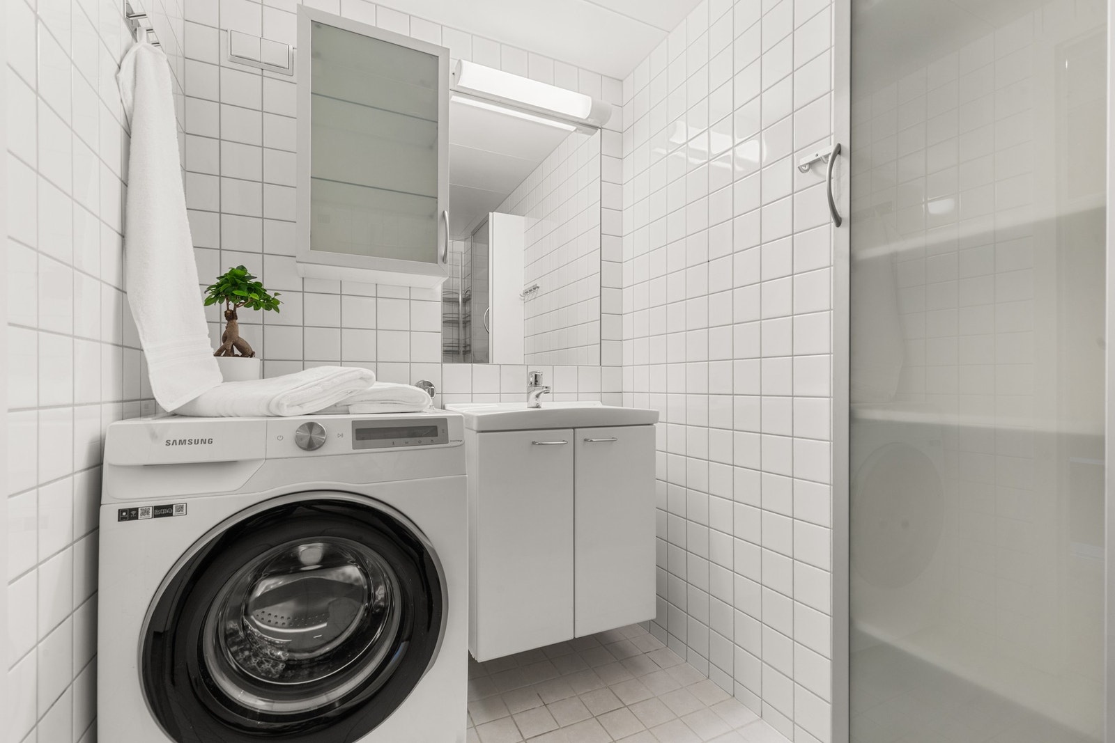 Her får du et lyst og flislagt bad med varmekabler i gulvet, servantinnredning med oppbevaringsplass og praktisk opplegg for vaskemaskin. Galleribilde