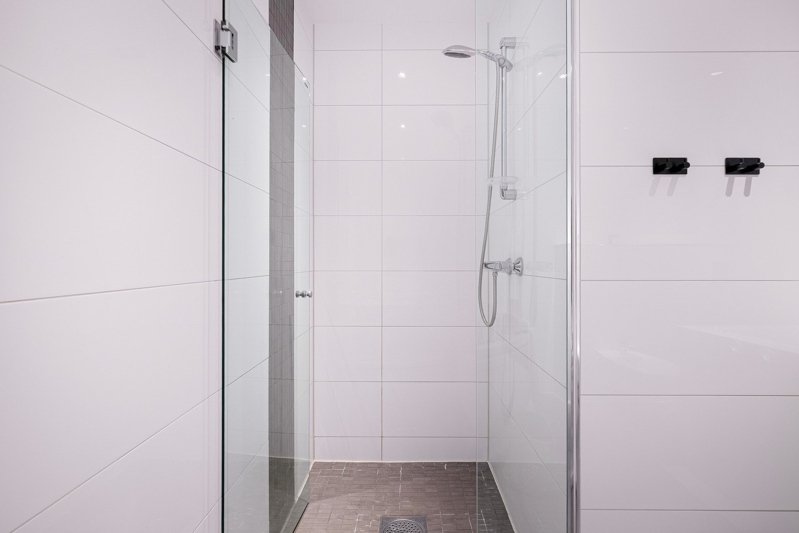 Badet er innredet med lyse fliser på vegger, mørkere fliser på gulv, servantinnredning, speilskap, vegghengt toalett, bidet, dusjsone med glassdør og badekar. Galleribilde