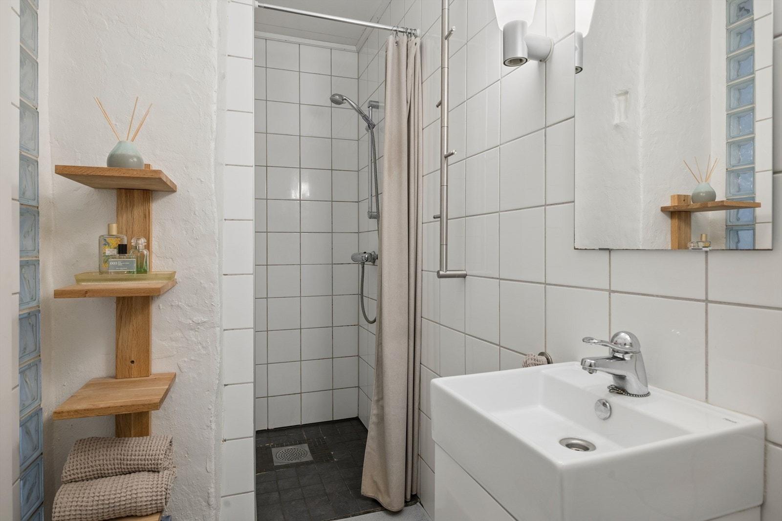 Badet er innredet med praktisk dusjnisje med veggmontert dusjgarnityr, gulvmontert toalett og servant med tilhørende innredning. Vaskemaskin befinner seg i nærliggende vaskerom i samme etasje. Galleribilde