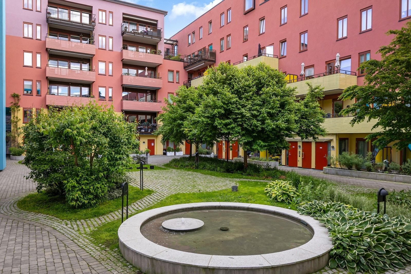 Gårdsrommet er pent opparbeidet med brostein, plen og beplantning. Galleribilde