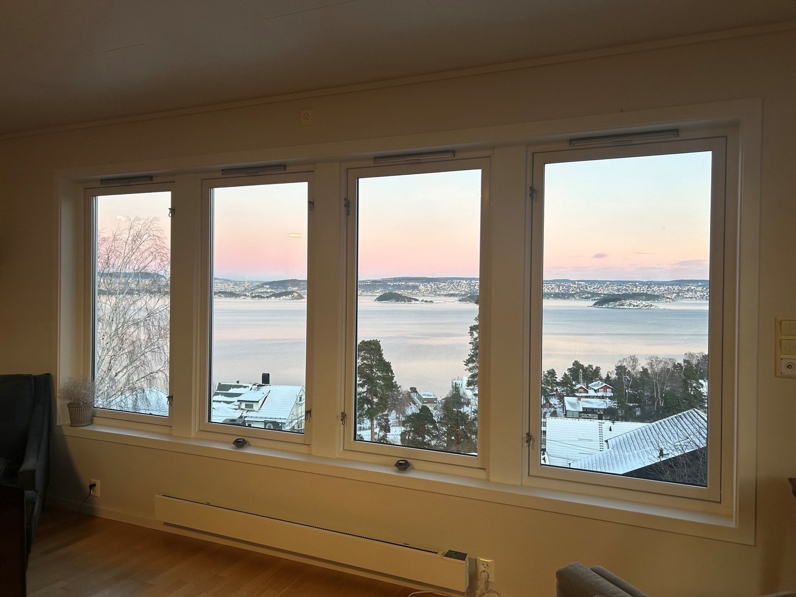 Selgers vinterfoto: Store vinduer i stuen gir flott utsikt mot Oslofjorden, med rosa lys og snødekte omgivelser som skaper en stemningsfull og unik atmosfære. Galleribilde