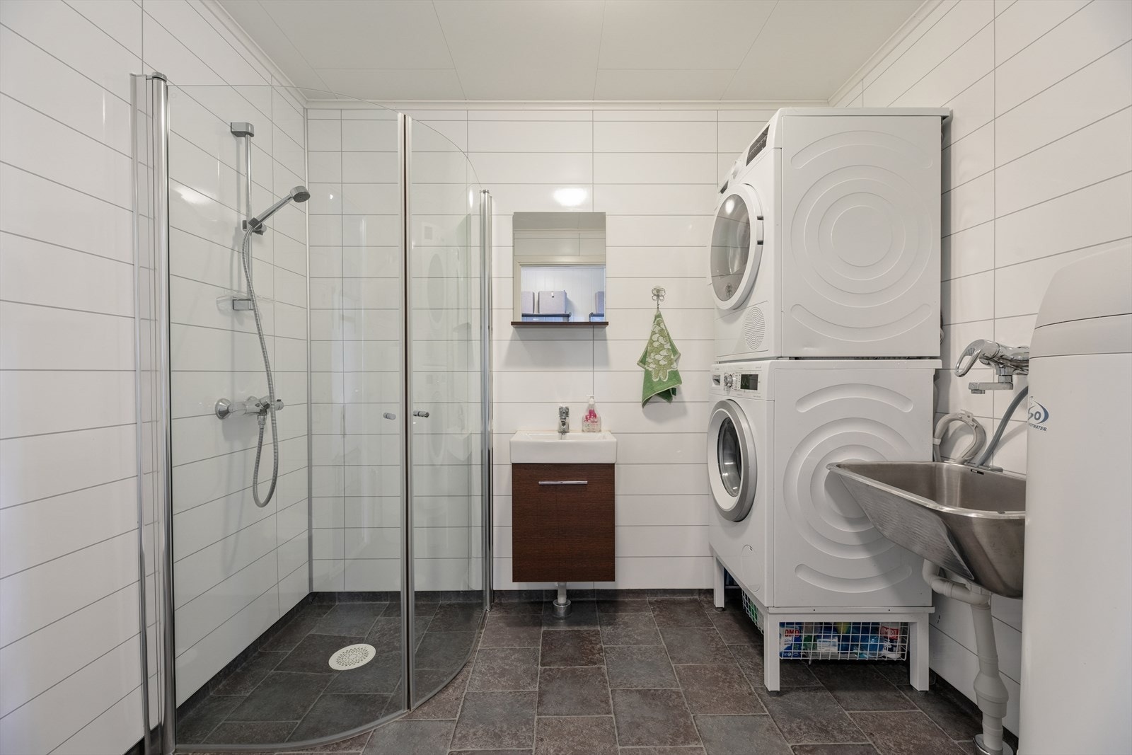 Bad-/vaskerom i første etasje. Praktisk beliggenhet ved entréen, her er vask, dusj, vegghengt toalett, opplegg for vaskemaskin, bereder og skyllekar. Vaskemaskin og tørketrommel kan medfølge handelen. Galleribilde