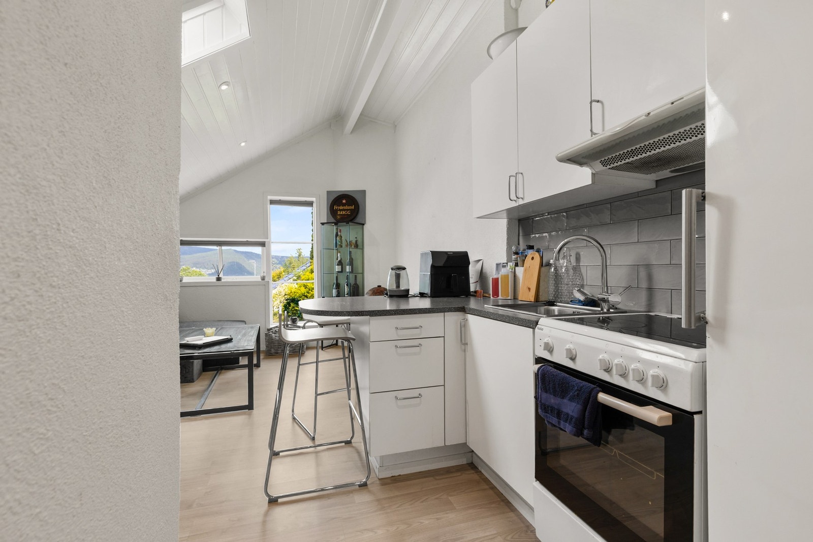 Kjøkken med innredning med glatte fronter og laminat benkeplate. Veggen over benkeplassen er flislagt, og kjøkkenet er utstyrt med ventilator med kullfilter Galleribilde