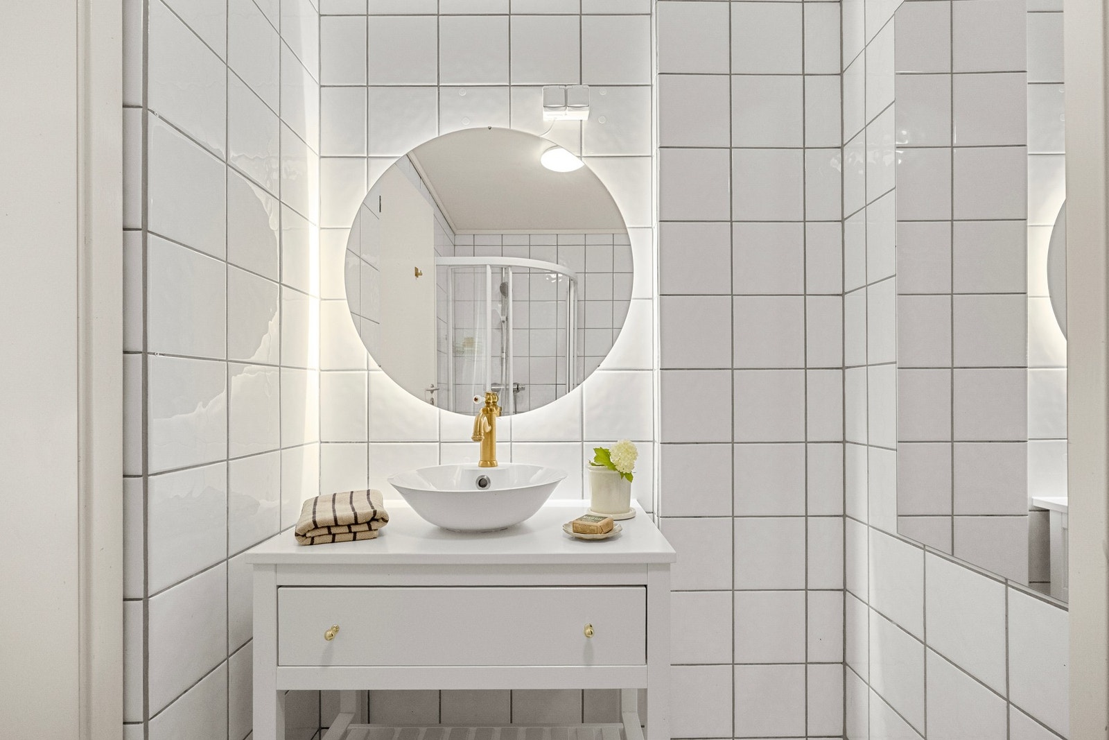 Badet har en funksjonell planløsning med flislagte overflater, dusjhjørne med glassvegger, servantinnredning og toalett. Galleribilde