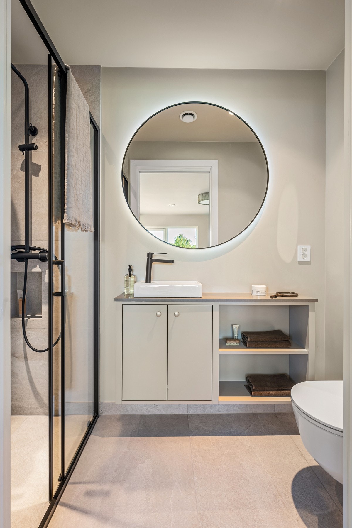 Det private badet ved hovedsoverommet har et stilrent uttrykk med flislagte overflater, servantinnredning, belyst speil og vegghengt toalett. Galleribilde
