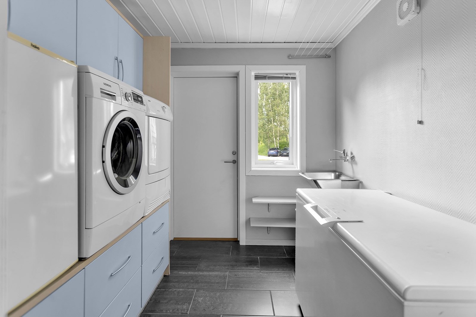 Praktisk vaskerom med flislagt gulv med gulvvarme, opplegg for vaskemaskin og egen utgang. Galleribilde