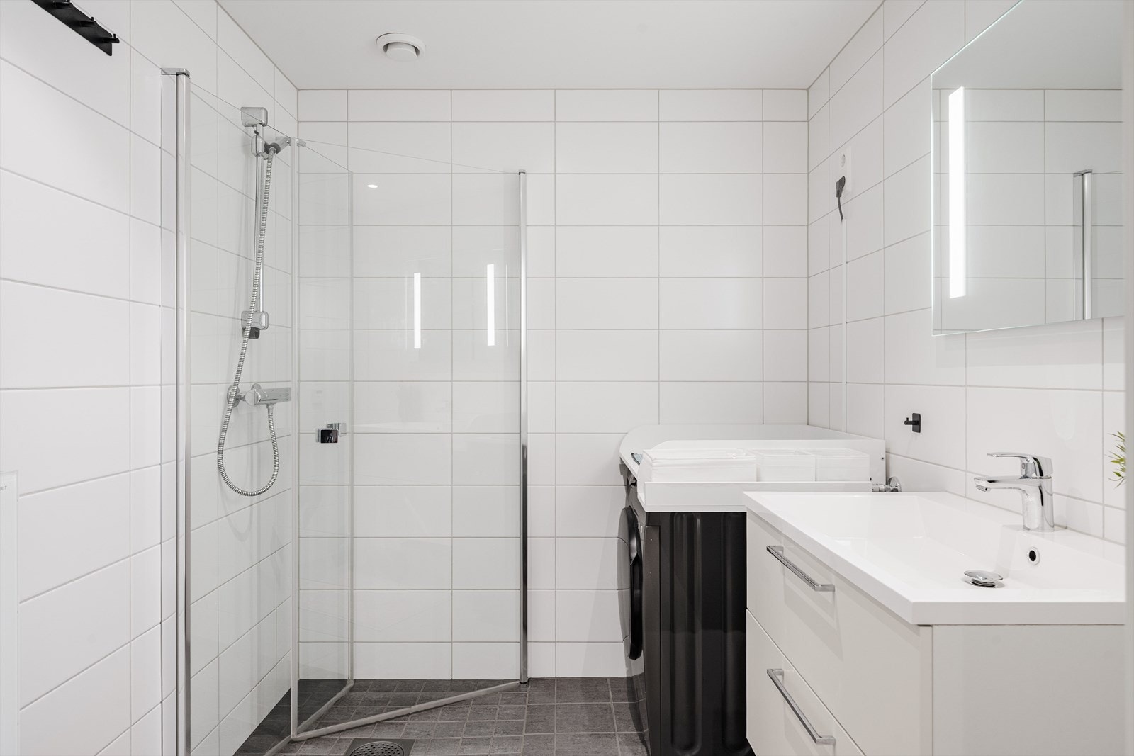 Leiligheten har et lyst og moderne baderom fra byggeåret 2019. Baderommet har grå fliser på gulv, vannbåren gulvvarme, lyse fliser på veggene, downlights i himlingen og avtrekk via balansert ventilasjon. Galleribilde