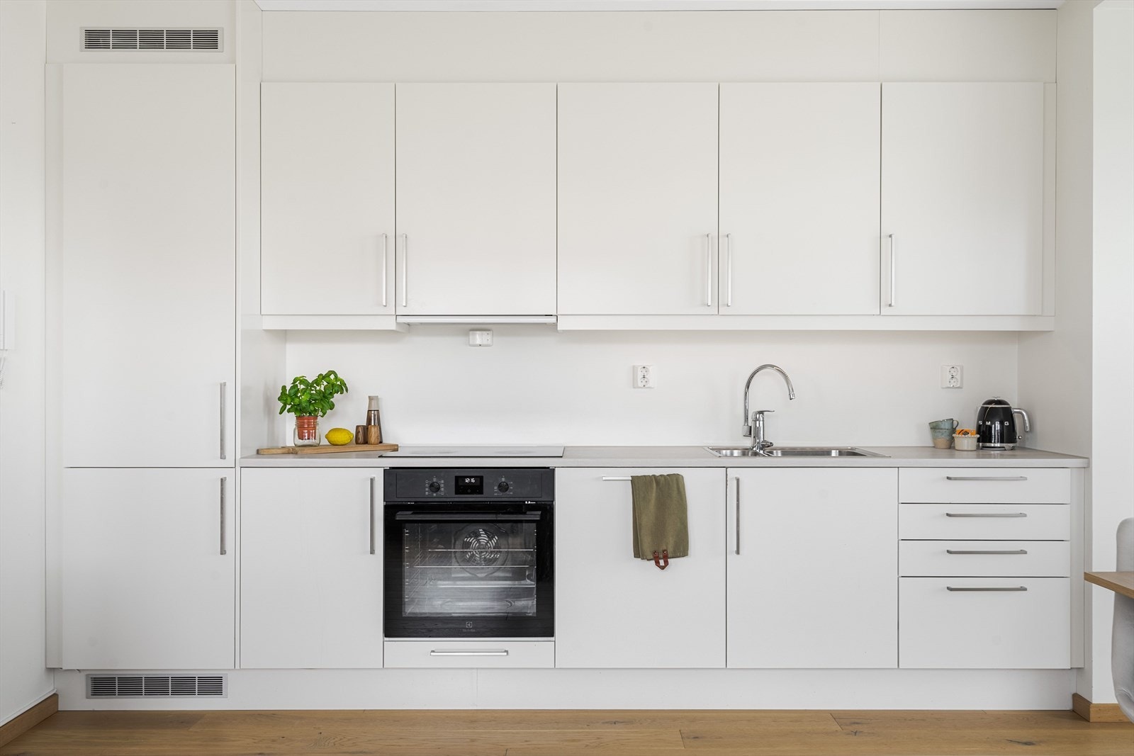 Innredningen har hvite glatte fronter og laminert benkeplate med nedfelt oppvaskkum. Praktisk med belysning under overskapene og kjøkkenventilator i overskap som drives av det balanserte ventilasjonsanlegget. Galleribilde