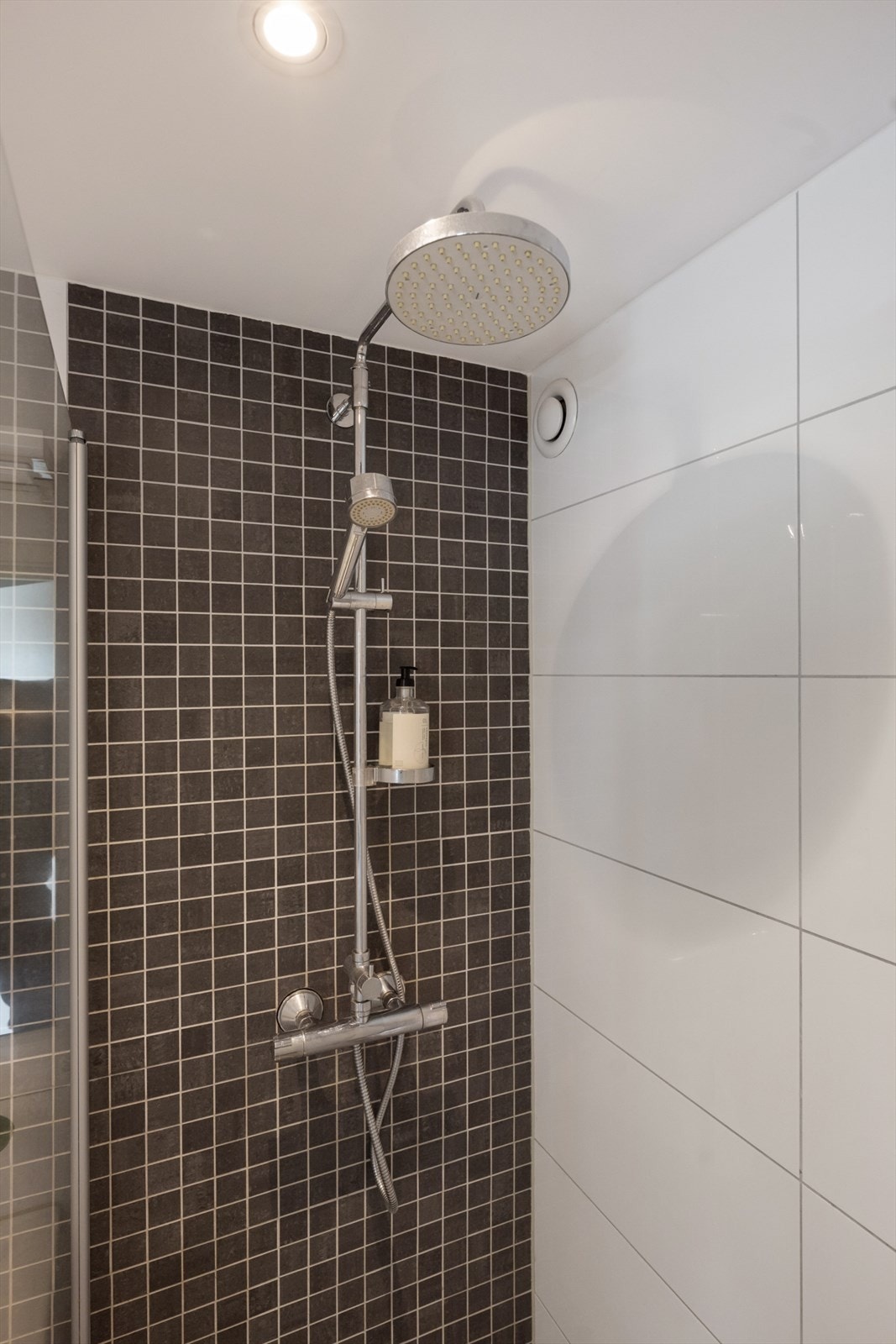 Badet er innredet med veggfestet toalett, servant i helstøpt plate med benkeskap, dusj på gulv med dører i herdet glass og opplegg for vaskemaskin. Galleribilde