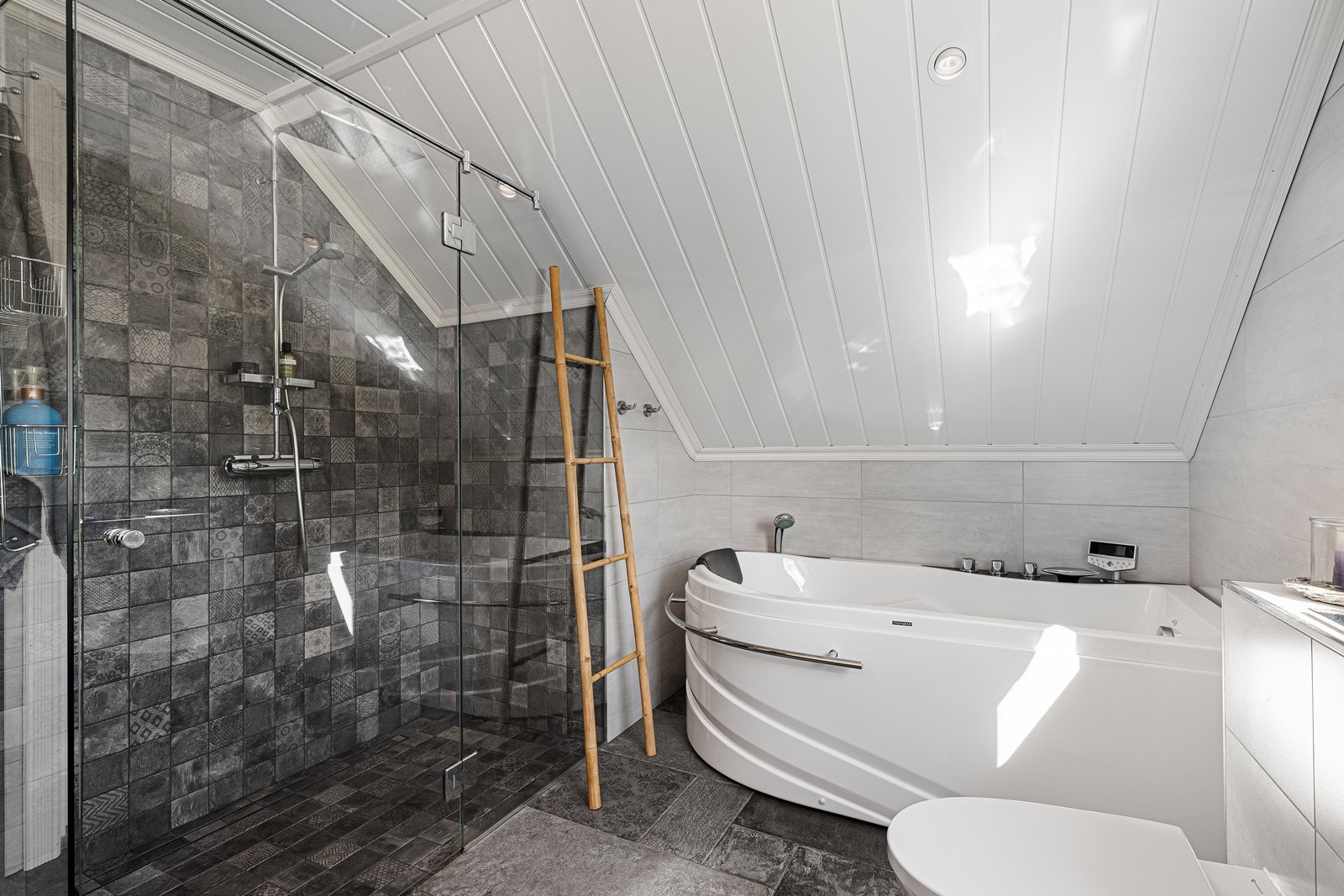 Badet er utstyrt med veggmontert toalett, badekar, glassvegger og dusjnisje med glassvegg samt dusjgarnityr. Galleribilde