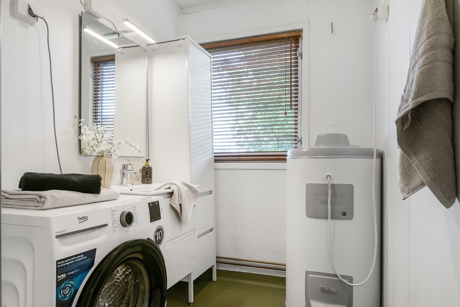 Badet fremstår praktisk innredet med servantinnredning, høyskap, dusjkabinett og opplegg for vaskemaskin. Galleribilde