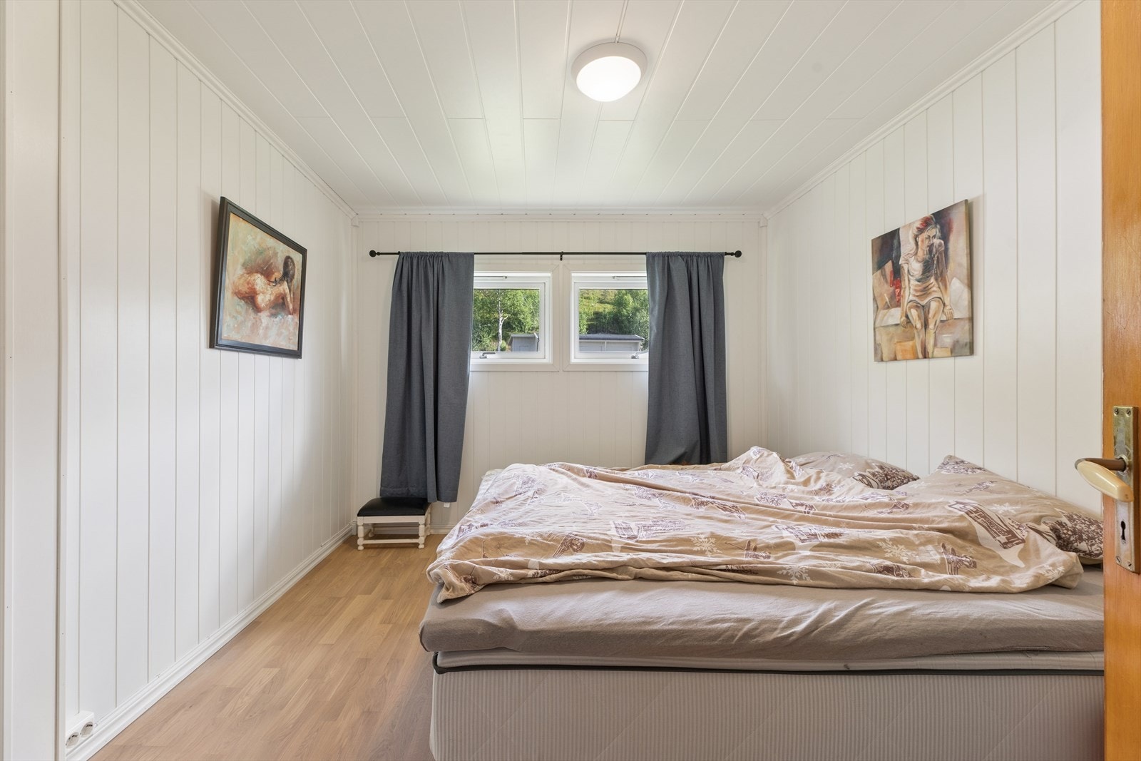 Et av soverommene i lofts etasje, med laminatgulv og malte panelplater. Galleribilde