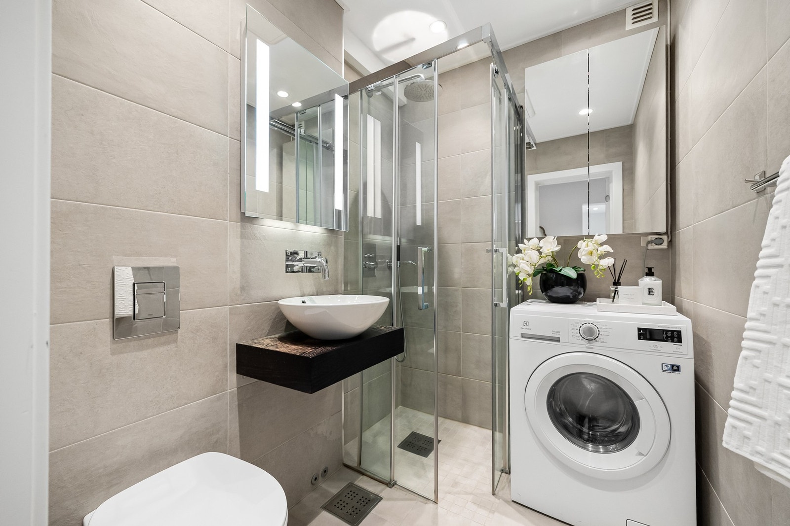 Flislagt bad med varmekabler i gulv. Badet er innredet med dusjnisje med skyvbare dusjvegger og integrert termostatstyrt dusjbatteri i krom med både hånd og regnfallsdusj. Galleribilde