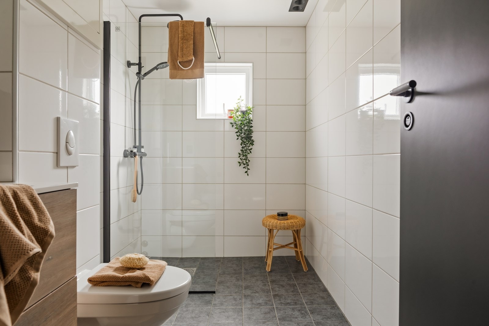Rommet er helfliset og innredet med delikat baderomsinnredning i trestruktur, sort armatur og romslig dusjsone med glassvegg. Galleribilde