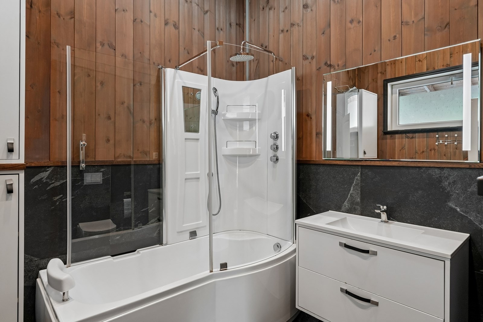 Badet ble oppgradert i 2020 og fremstår moderne og praktisk. Badet er utstyrt med servantinnredning, speil, vegghengt toalett og dusjkabinett med badekar og glassdør. Galleribilde