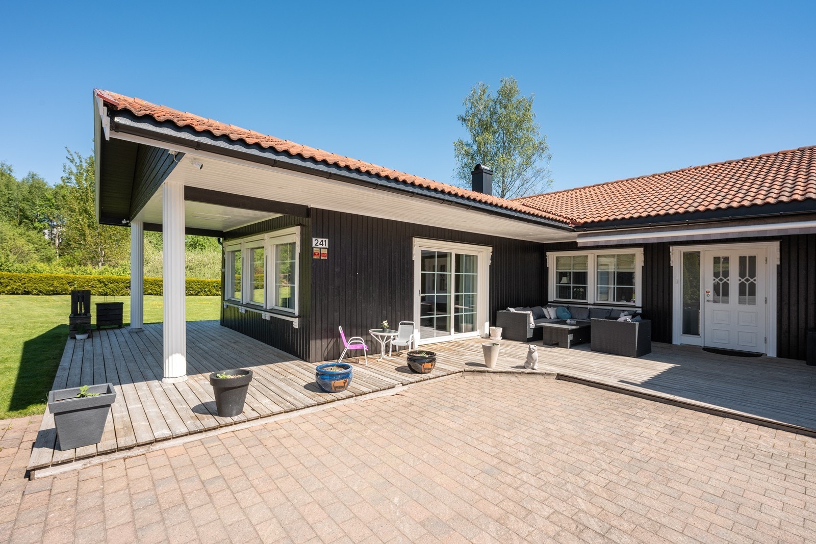 Det pene inngangspartiet ligger tilknyttet terrasse og har hvit inngangsdør med glasspartier og et langsgående glassfelt. Galleribilde