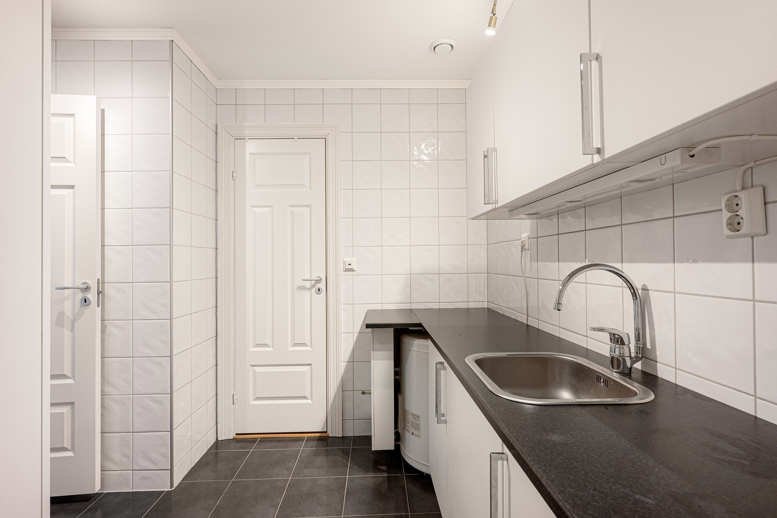 Vaskerommet har hvit innredning med glatte fronter, mørk laminatbenkeplate med nedfelt oppvaskkum i metall, overskap, samt egen plass for vaskemaskin. Galleribilde