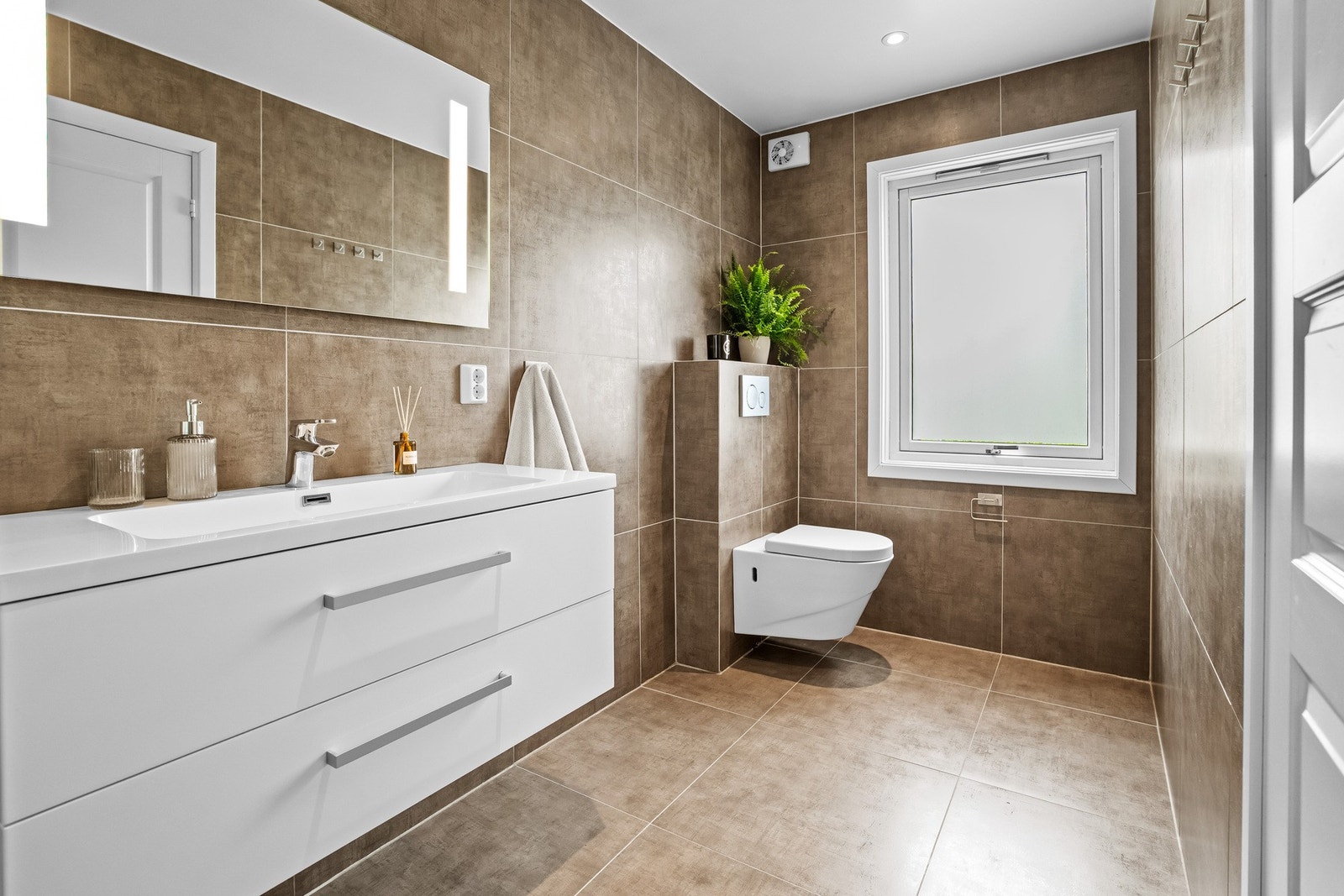 Badet er innredet med servantmøblement, speil med integrert belysning samt en egen dusjnisje med glassvegg og glassdør. Galleribilde