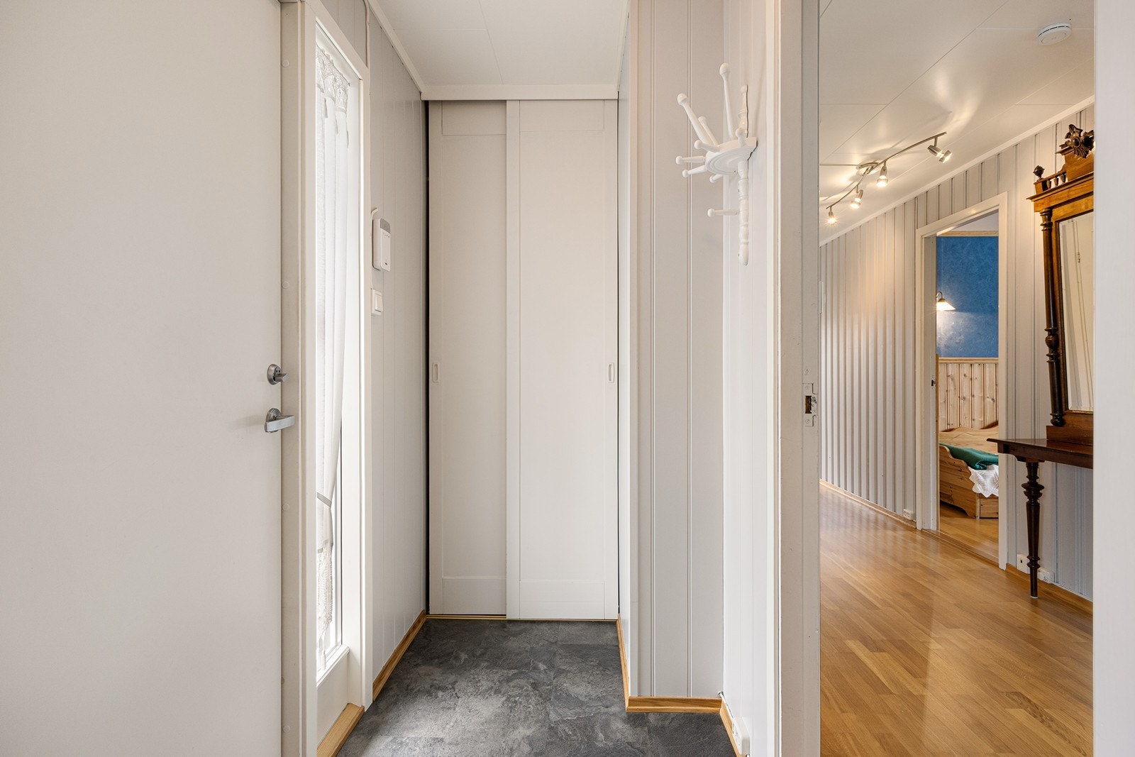 Entréen har lyse veggflater som står godt til flislaminatet i gråtoner på gulvet. Yttertøyet ryddes enkelt bort i en plassbygd skyvedørsgarderobe - i tillegg er det knaggrekke. Galleribilde