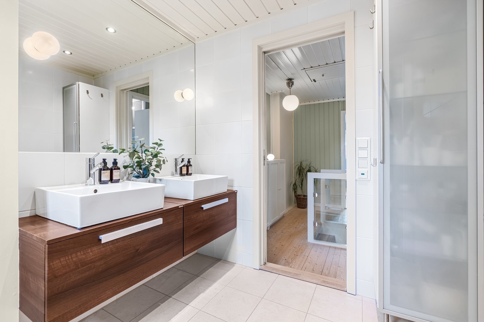 Badet har to servanter på felles innredning med mørke fronter, speil, veggskap, klosett og dusj med glassdører. Galleribilde