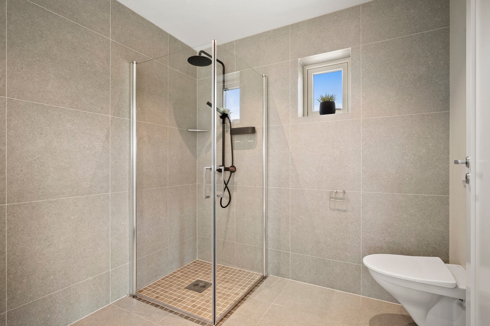 Badet er utstyrt med dusj med glassvegger, servantseksjon med skuffer, speil med lys og WC. Galleribilde