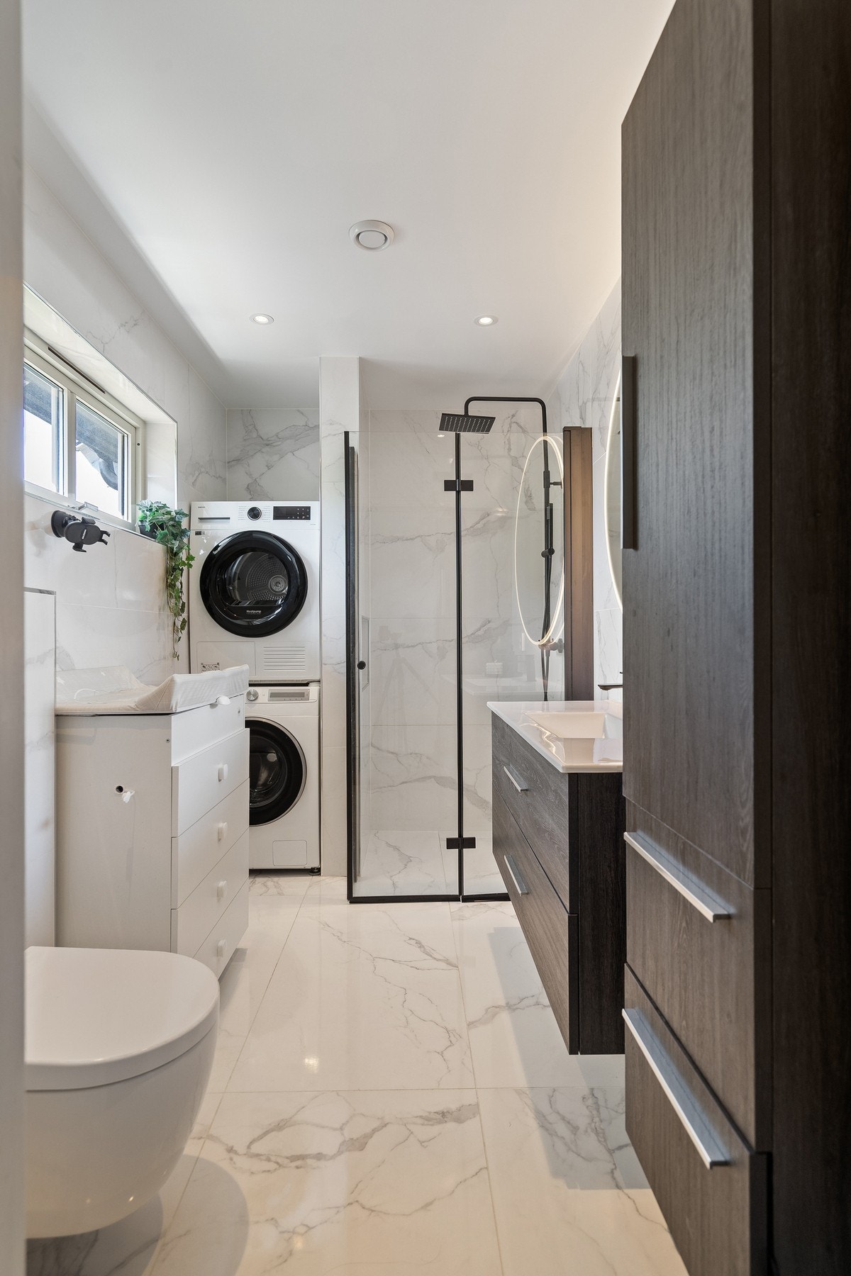 Badet er innredet med romslig dusjsone med glassvegger, flott baderomsinnredning med god oppbevaringsplass og et elegant, belyst speil som skaper en eksklusiv hotellfølelse. Galleribilde