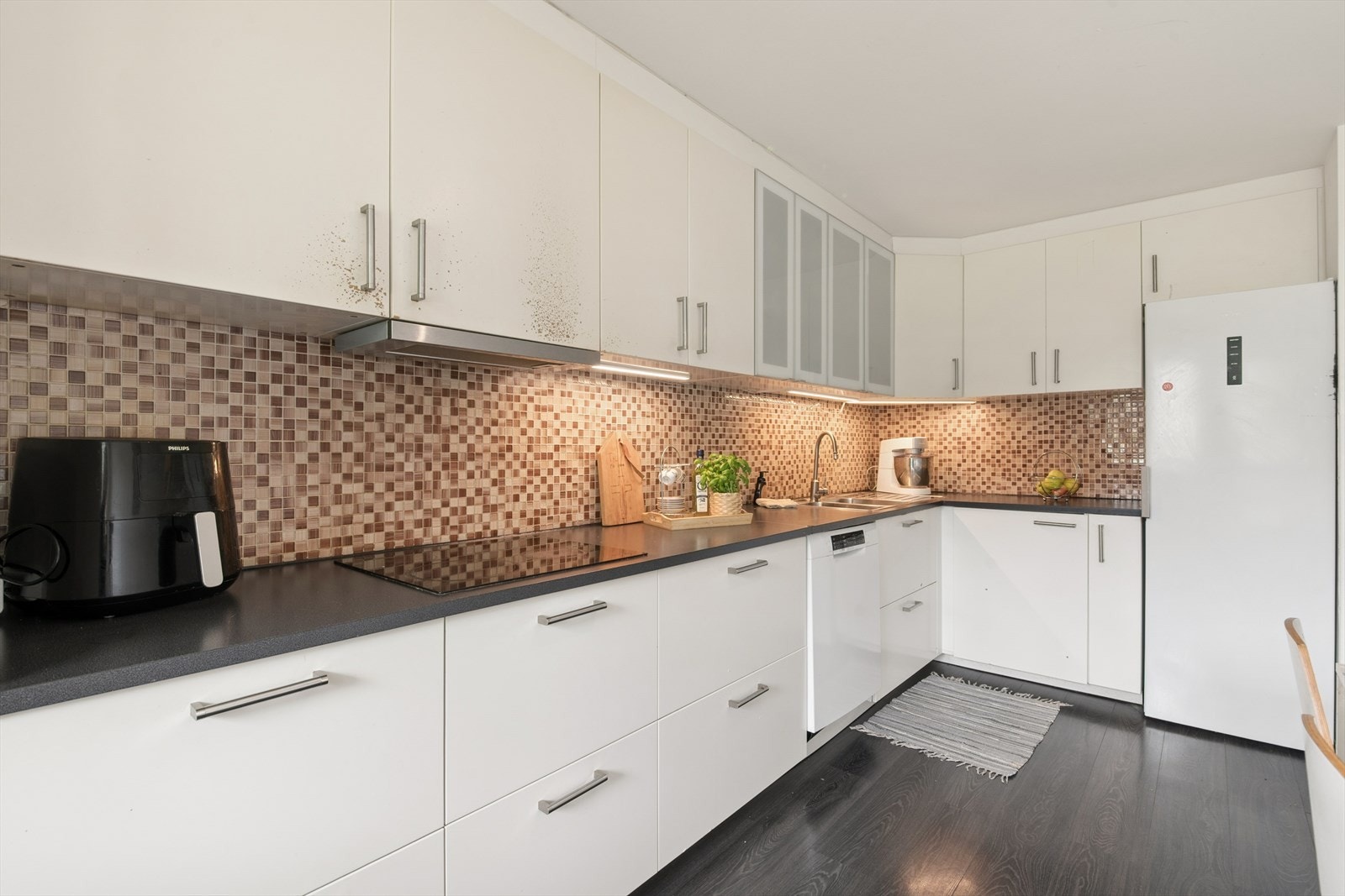 Kjøkkenet er innredning med glatte fronter, fliser på vegg over benkeskap og benkeplate av laminat. Galleribilde