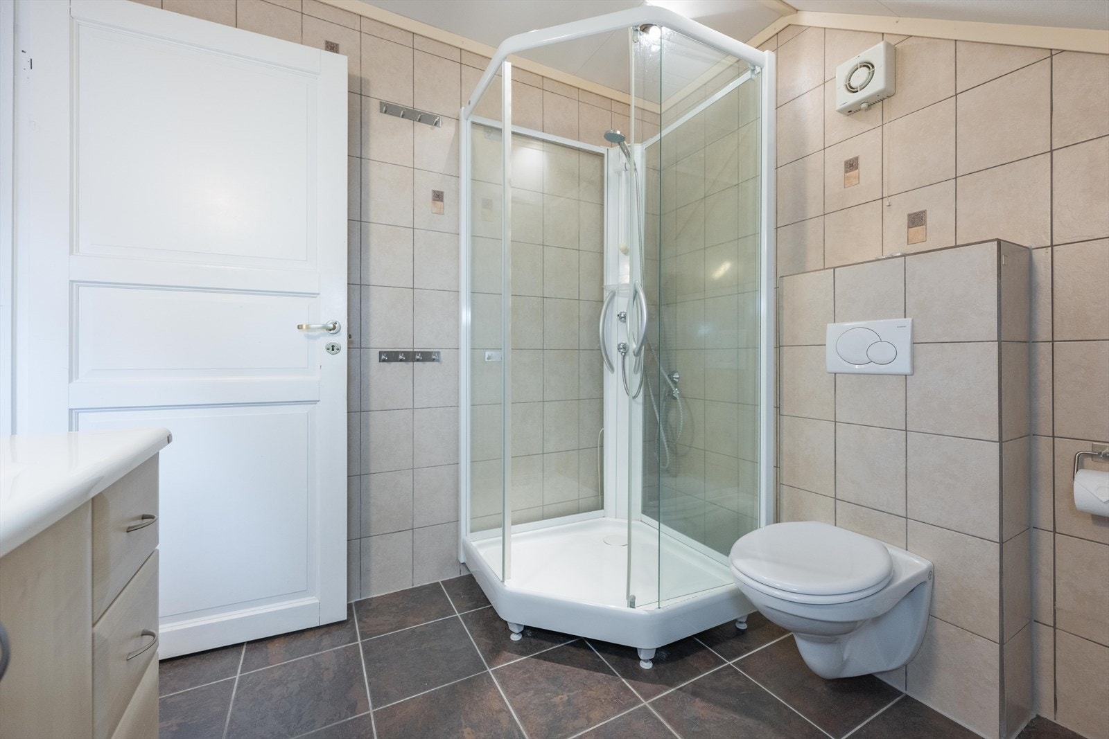 Badet er utstyrt med vegghengt toalett, dusjkabinett og servant med undermøblering Galleribilde