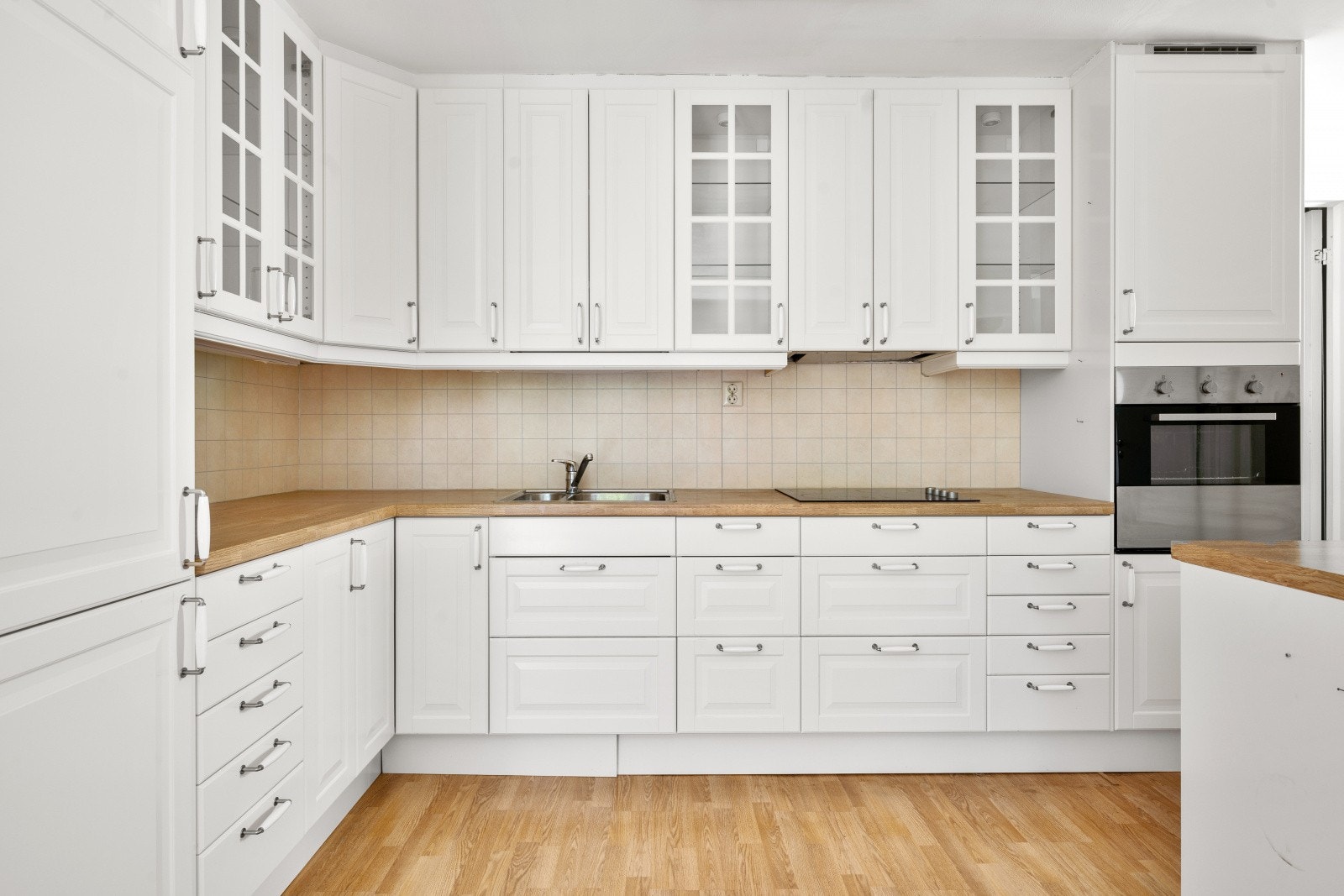Innredningen er fra IKEA (ca. 2012) og har hvite, profilerte fronter som gir et tidløst og klassisk uttrykk. Vitrineskapene tilfører et elegant preg og gir mulighet for å vise frem servise og glass på en dekorativ måte. Galleribilde